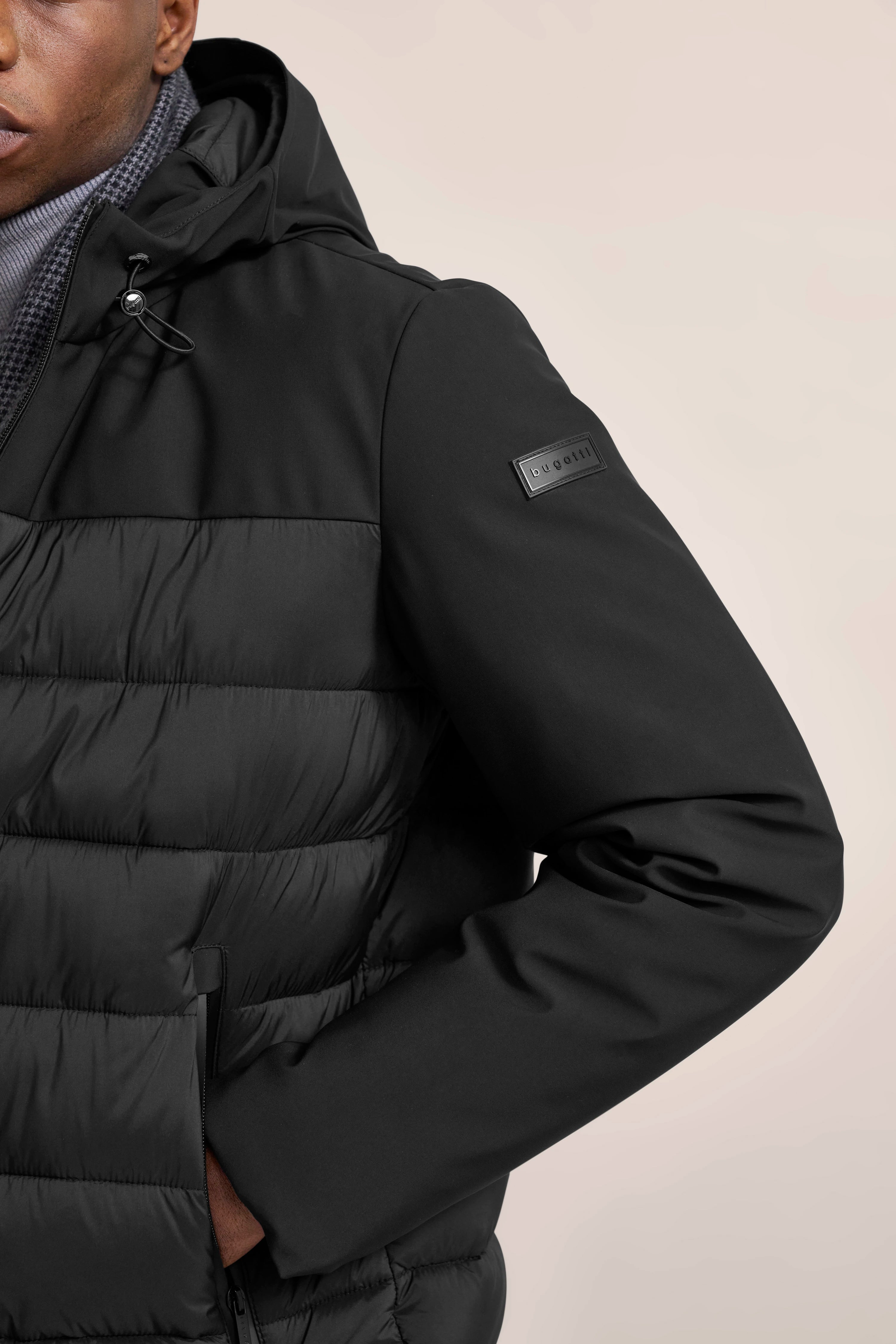 Schwarze bugatti Jacke im legeren Bild, Detailaufnahme mit Kapuze und Logo.