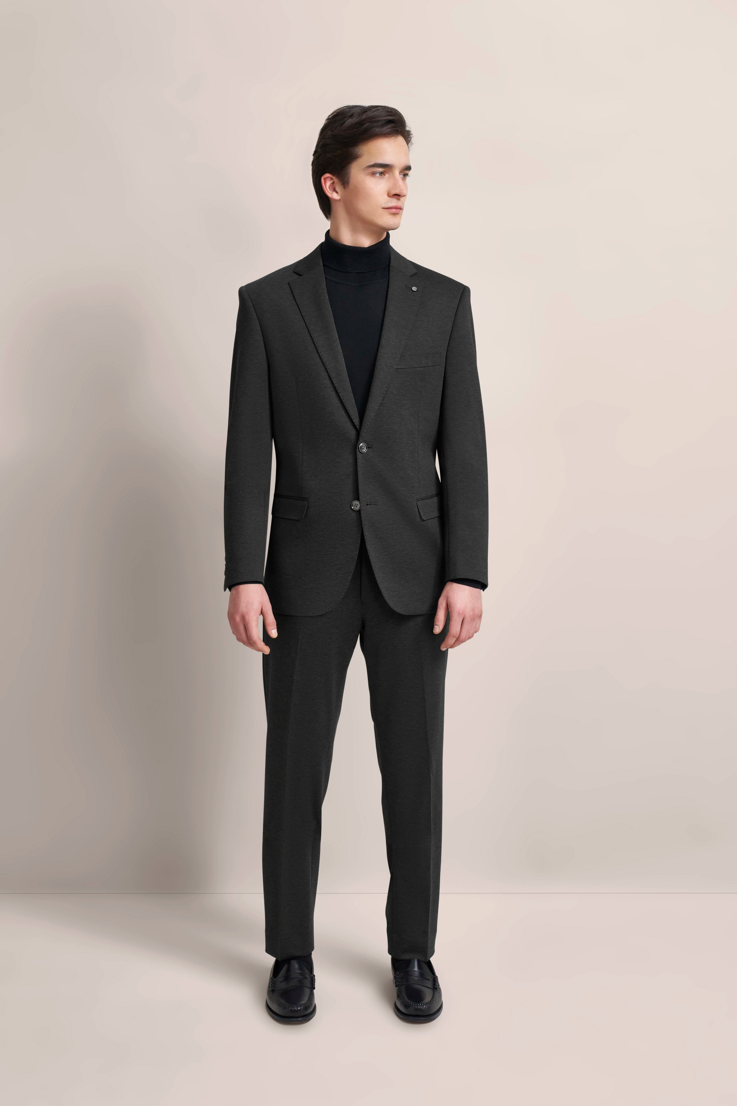 Man in gray bugatti suit, black turtleneck, posing formally.