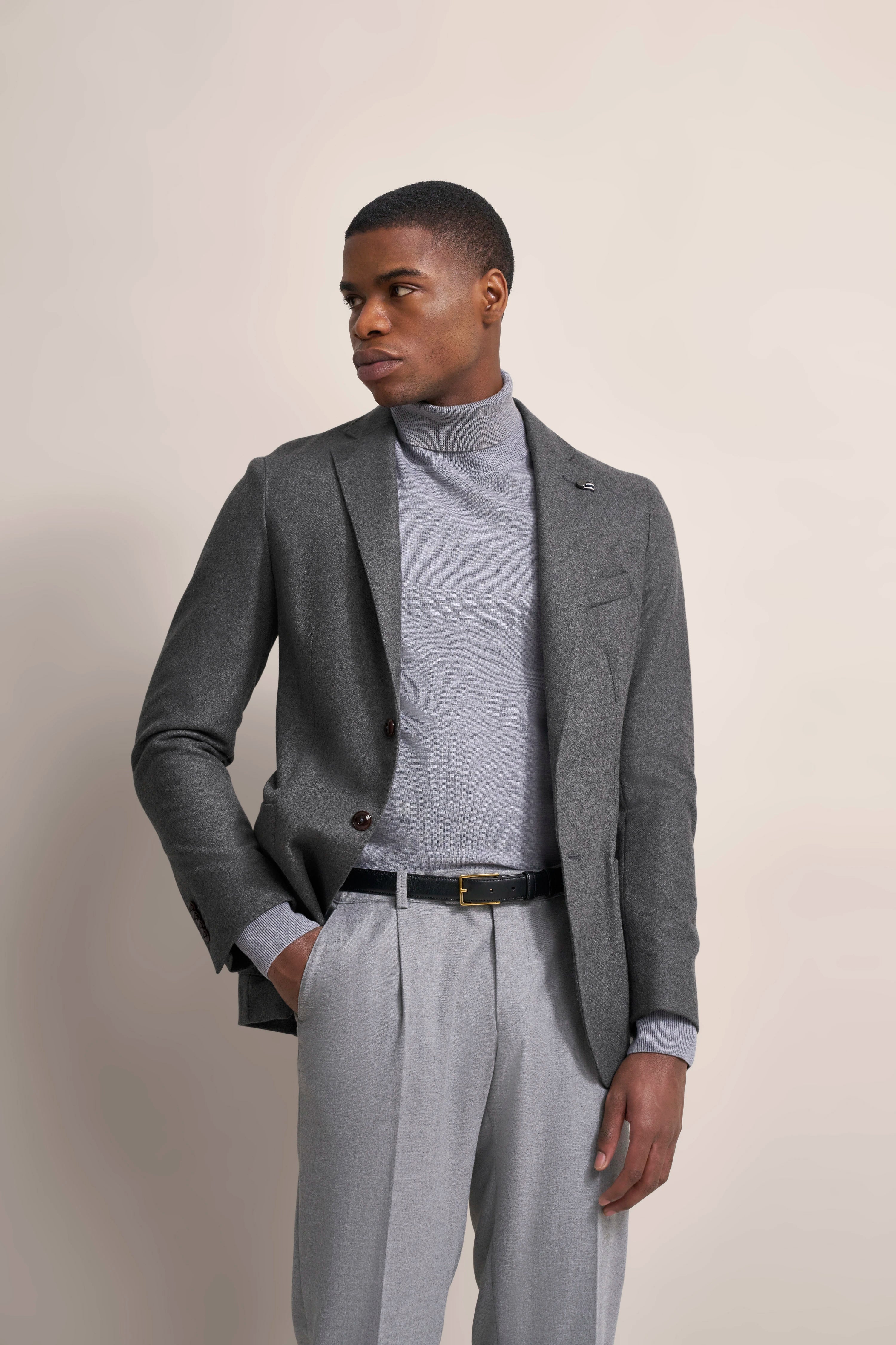 Person in grauem Blazer, Rollkragenpullover und Hose, Modellbild, entspannte Pose.