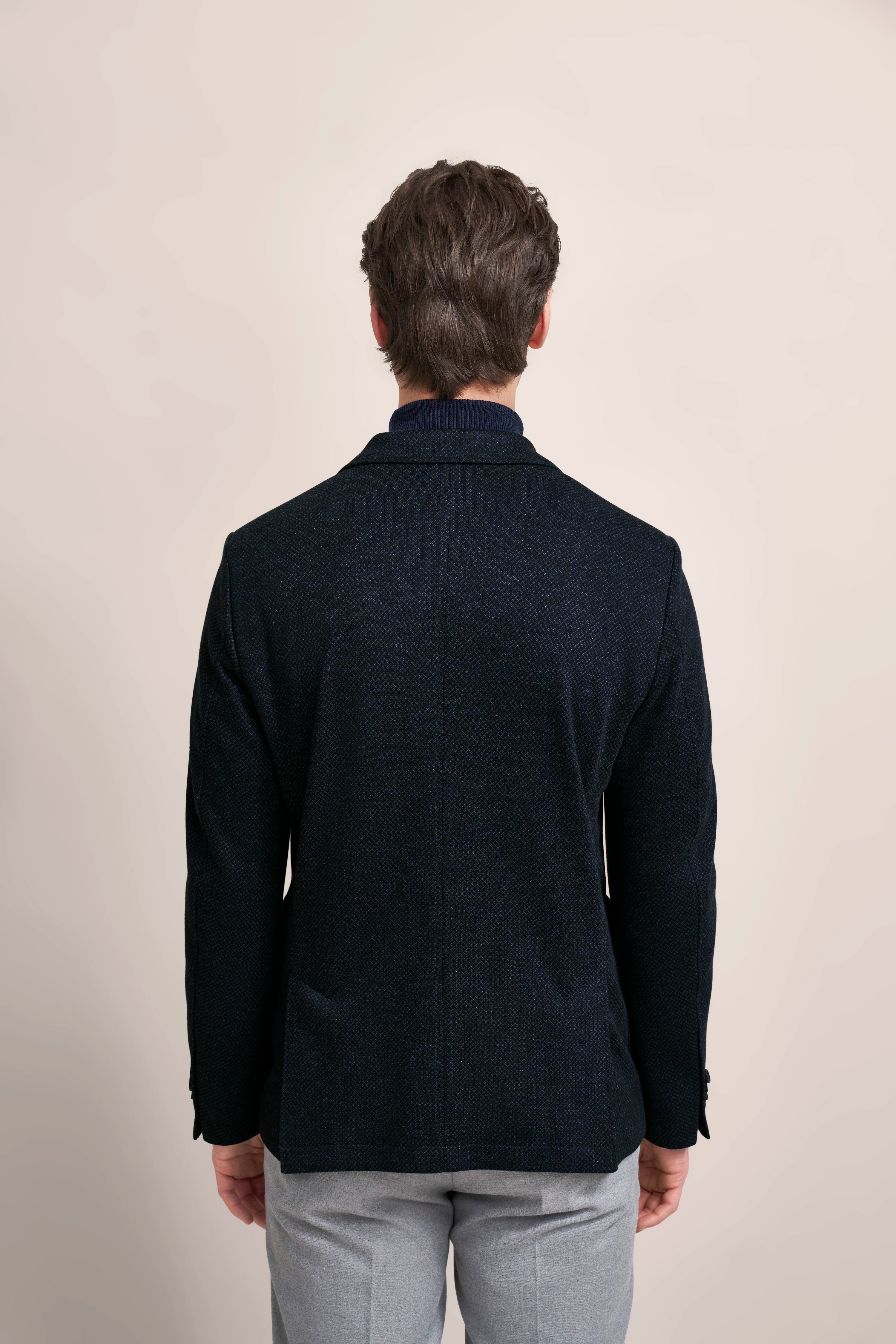 bugatti Modelbild, Rückansicht: Dunkler Blazer mit feiner Struktur, kombiniert mit grauen Hosen, entspanntes Posing.