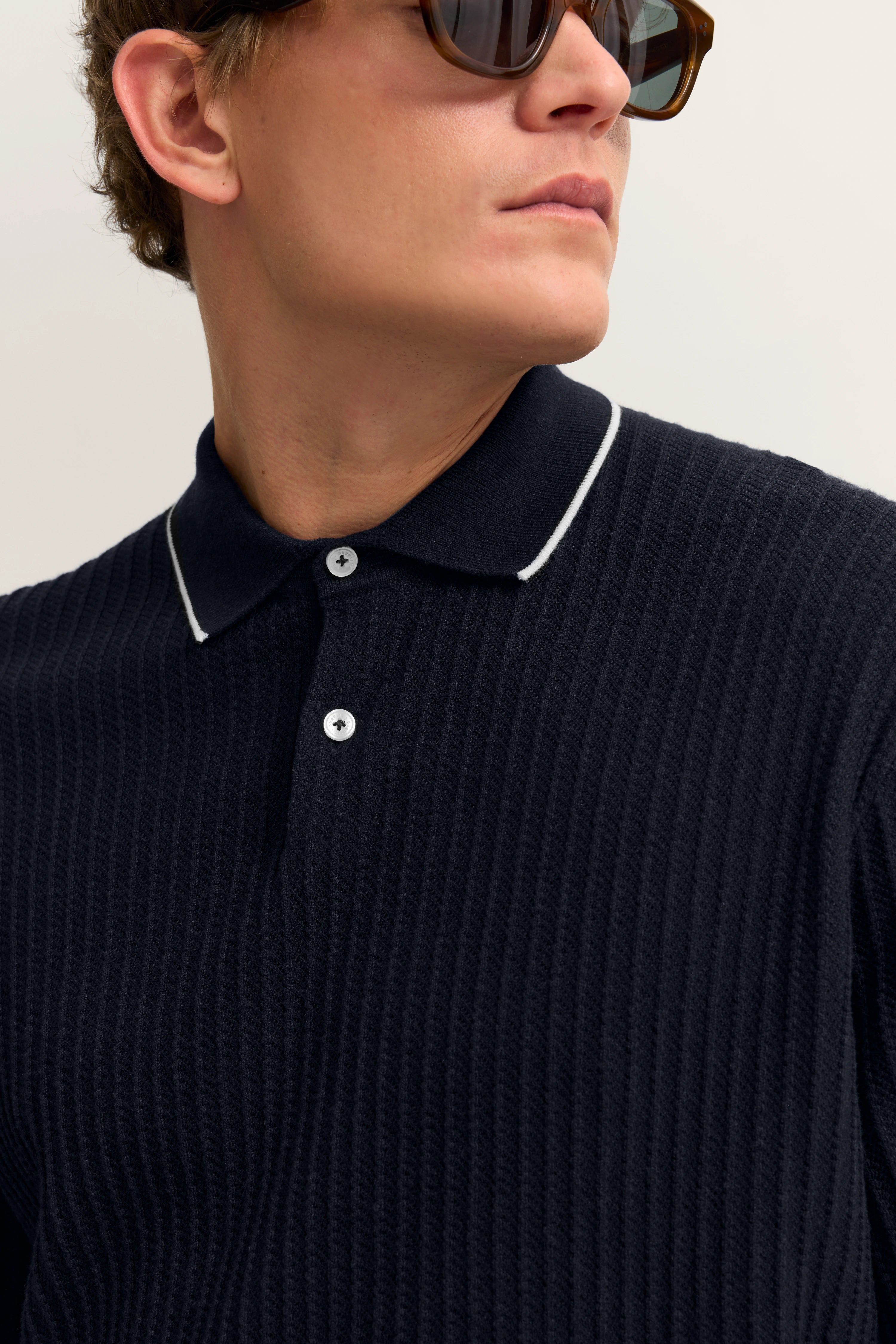 Navy Poloshirt mit feiner Struktur, getragen von einem Model mit Sonnenbrille, Büstenbild.