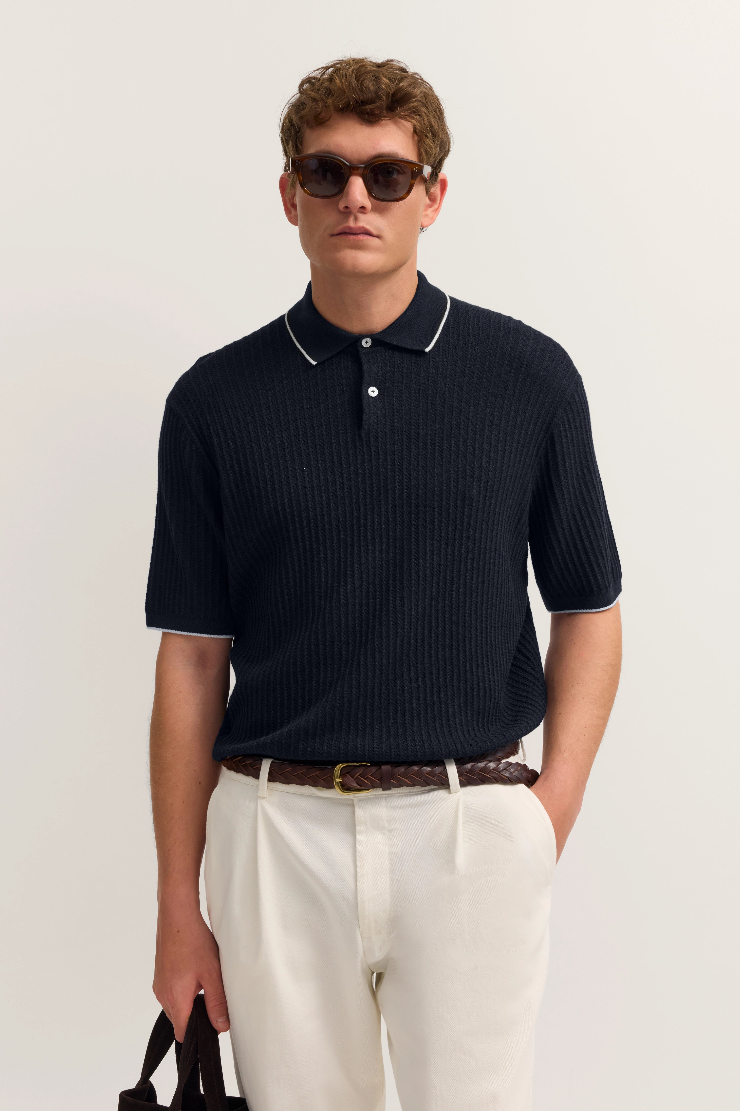 Modelbild mit schwarzem bugatti-Polo und weißer Hose, lässige Haltung, Sonnenbrille.