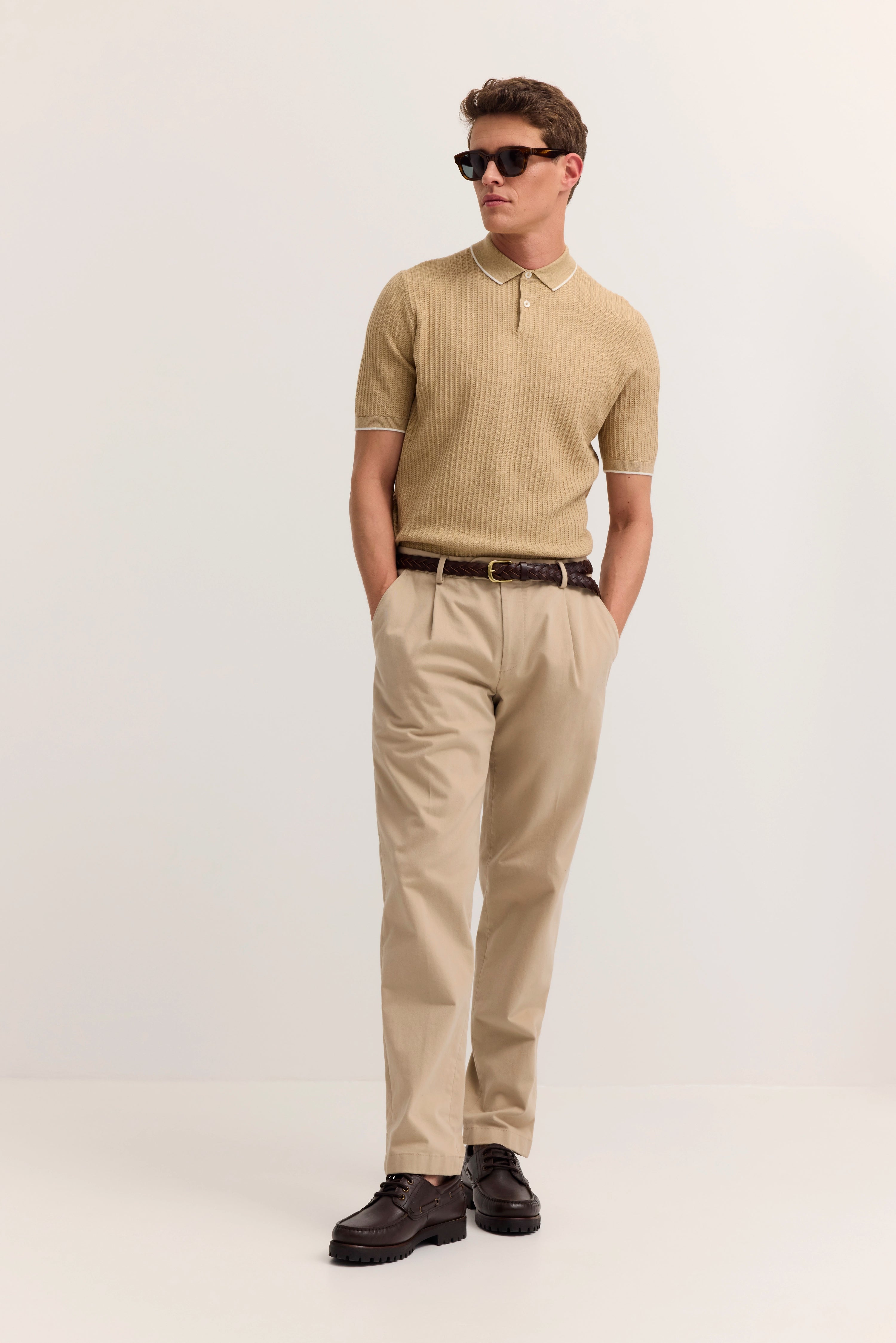 Beiges Polo und Chinos, brauner Gürtel, Modelbild in lässiger Pose.