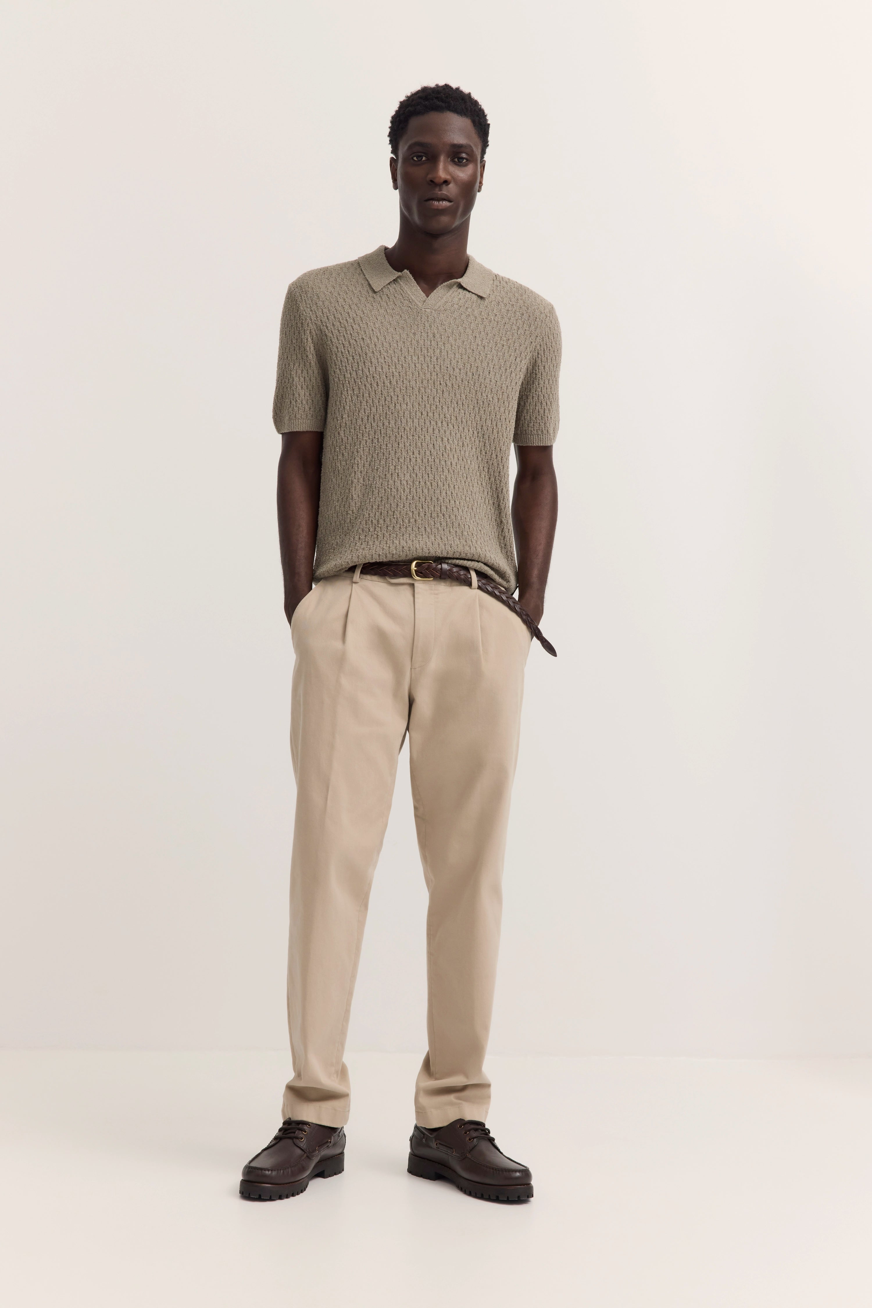Beiger Strickpolo und Chinos, legeres Modelbild, entspannte Pose.