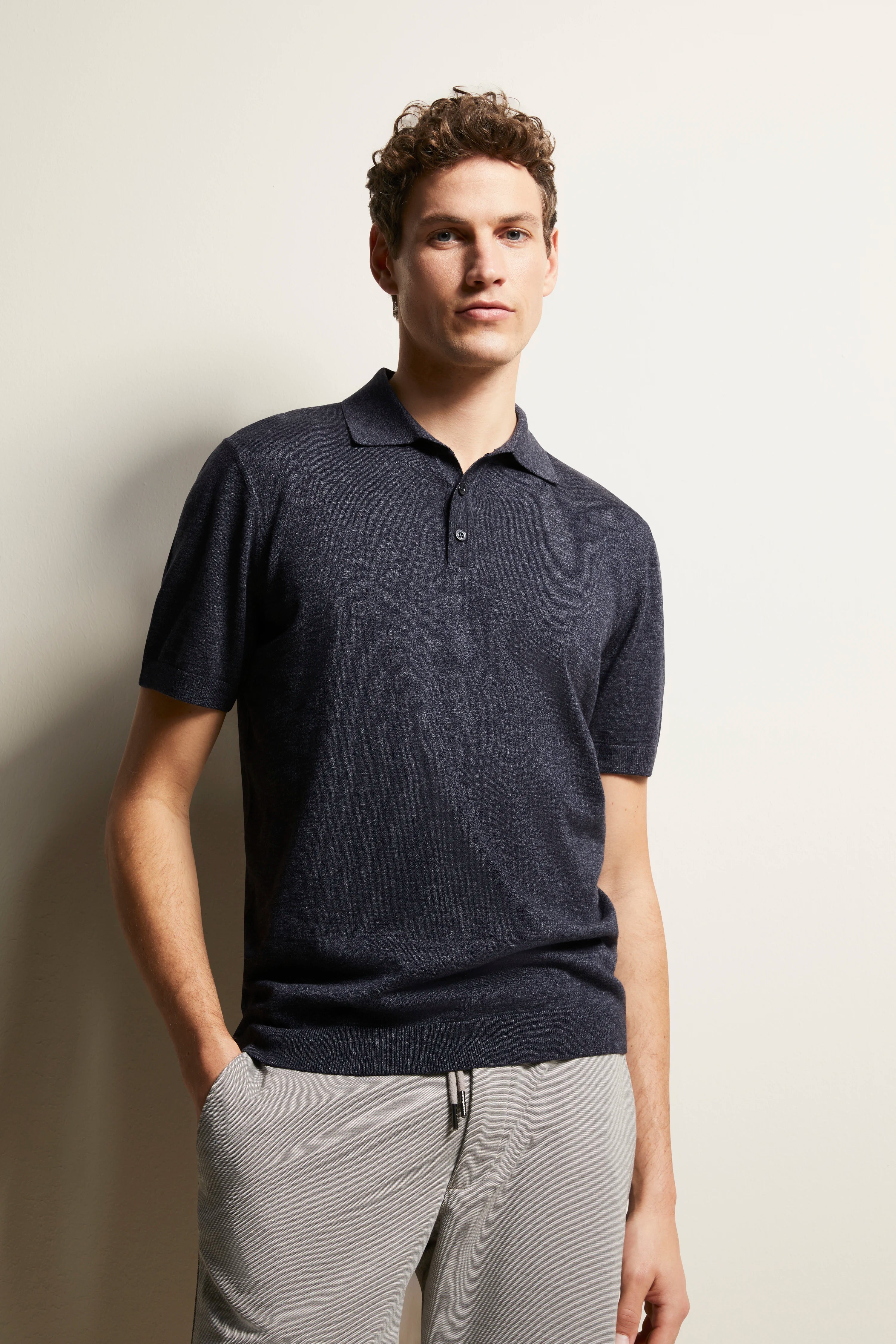 Model trägt navy Polohemd und graue Hose von bugatti, legeres Posing, linke Hand in Hosentasche.