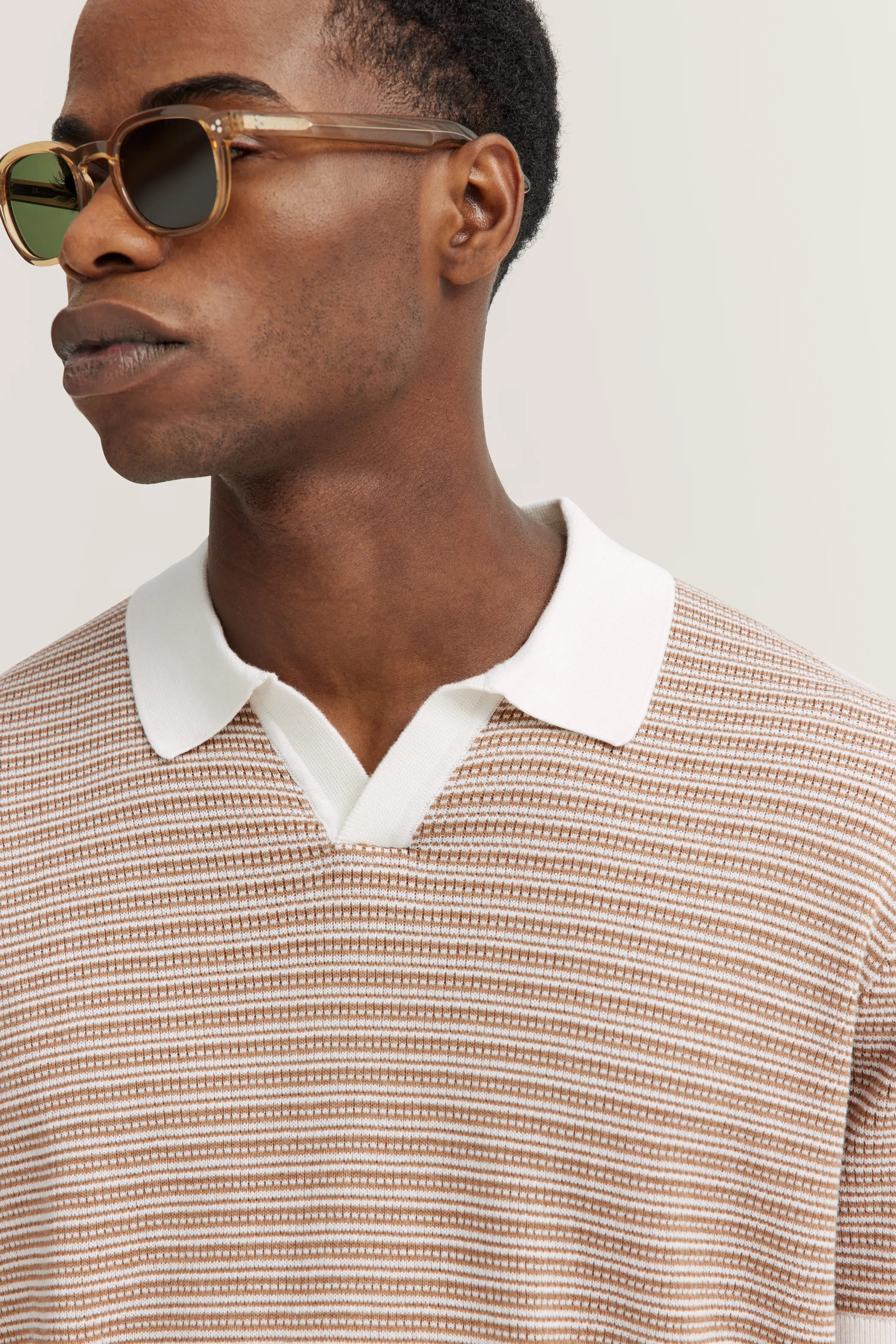 Beigefarbenes Poloshirt mit Streifenmuster, Close-up-Bild, Modell mit Sonnenbrille.