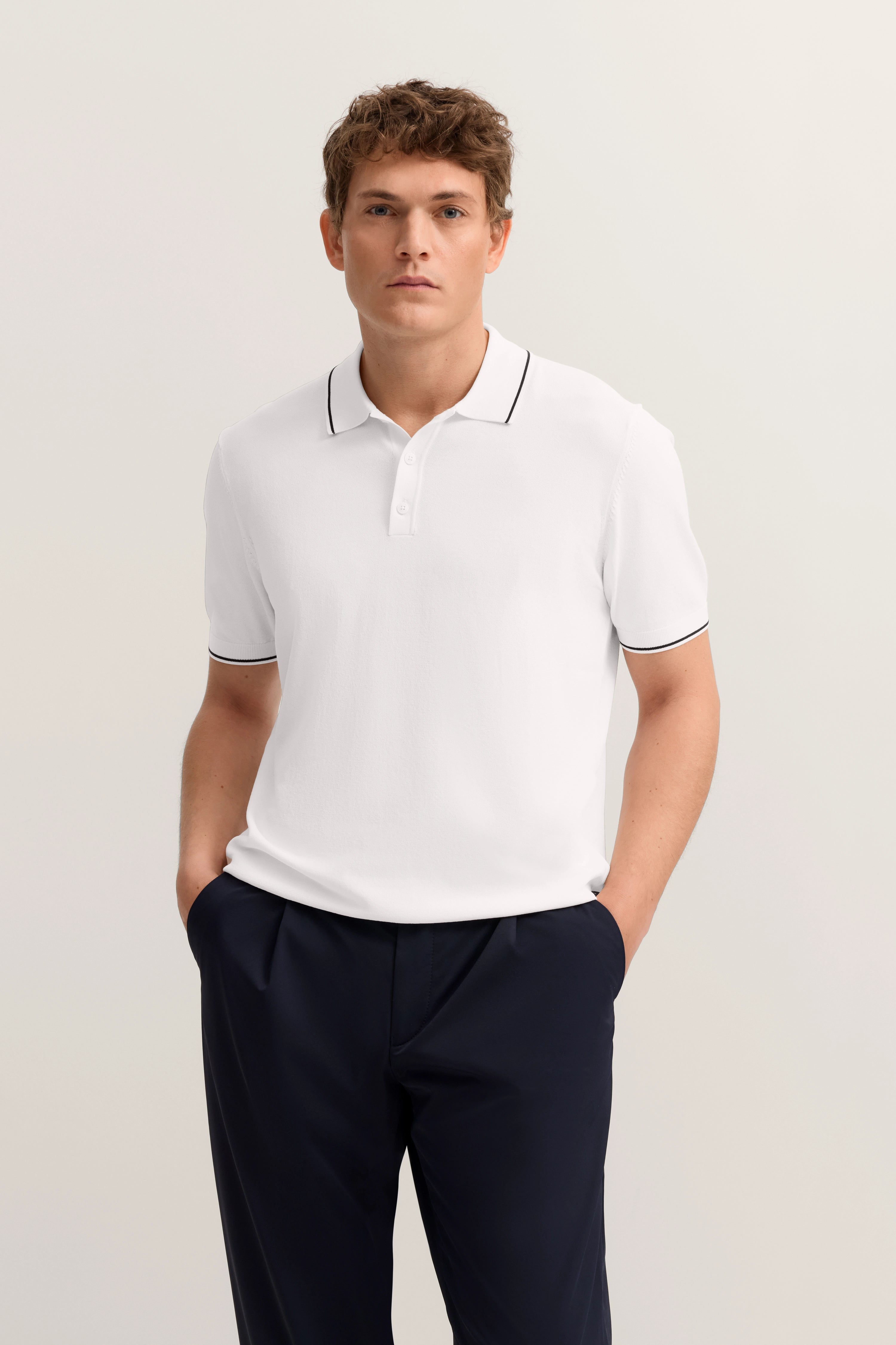 Weißes Polohemd mit schwarzer Paspel, dunkelblaue Hose, Modelbild, entspannte Pose.