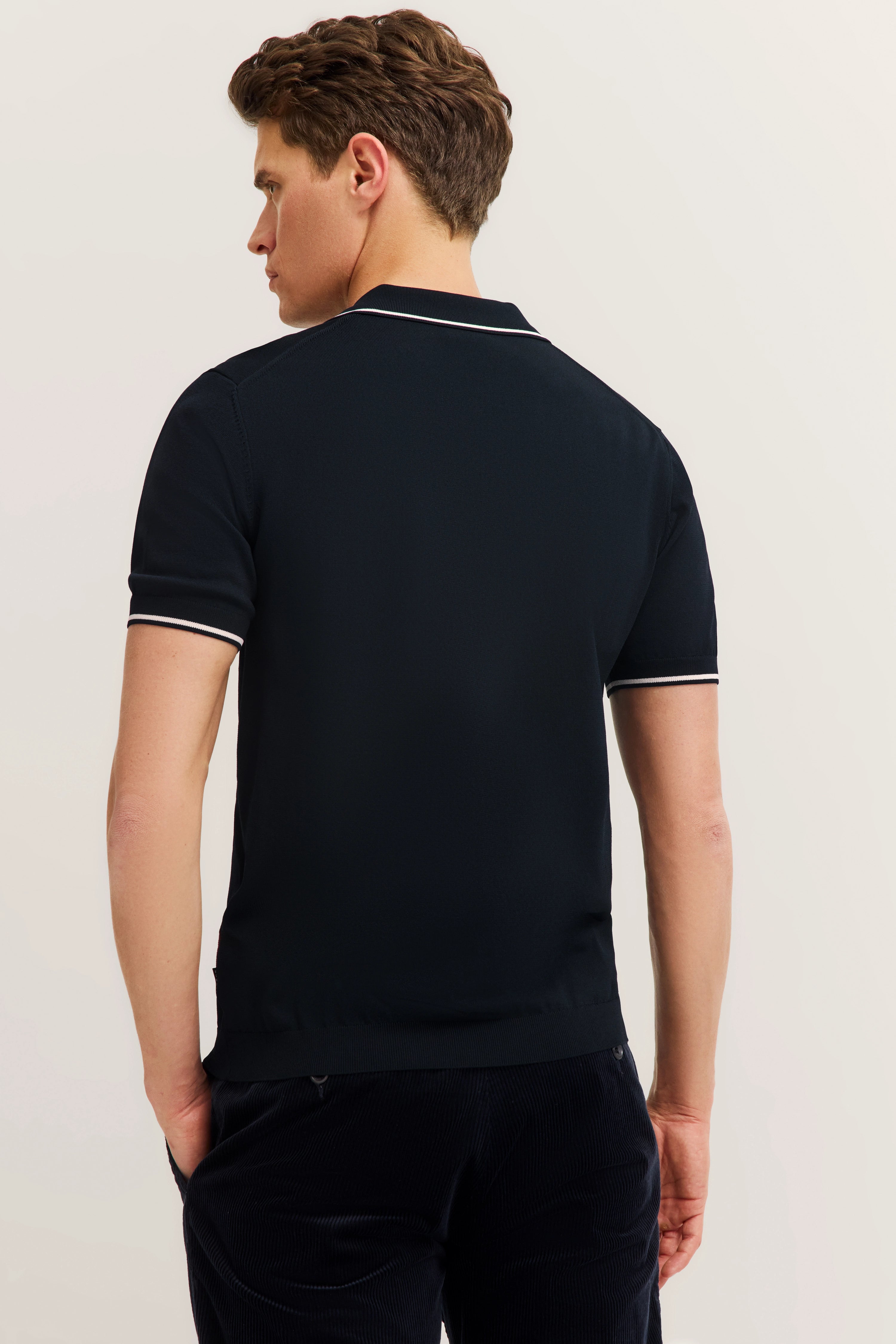 Mann in dunkelblauem bugatti Polo und Hose, Rückansicht, legeres Modelbild.