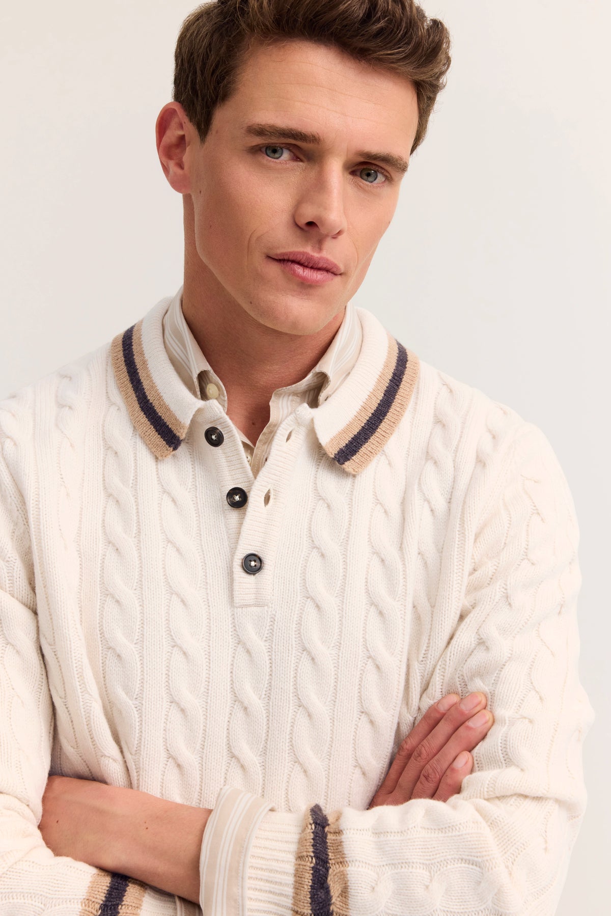 Bugatti Modell in cremefarbenem Strickpullover mit Zopfmuster und gestreiftem Kragen, lässige Pose.