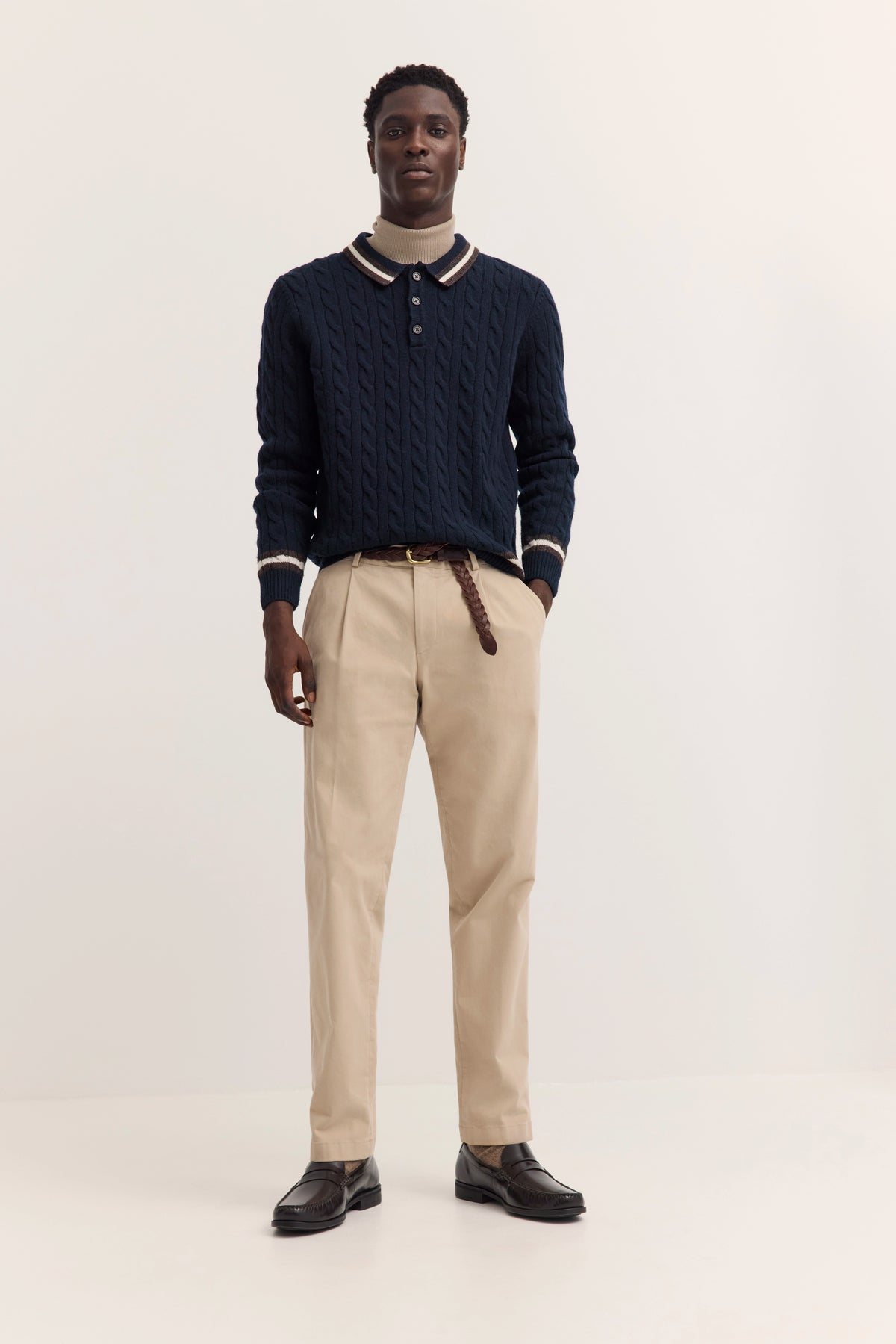 Dunkelblauer Zopfmuster-Pullover mit beigem Rollkragen, Modelbild mit ernstem Ausdruck.