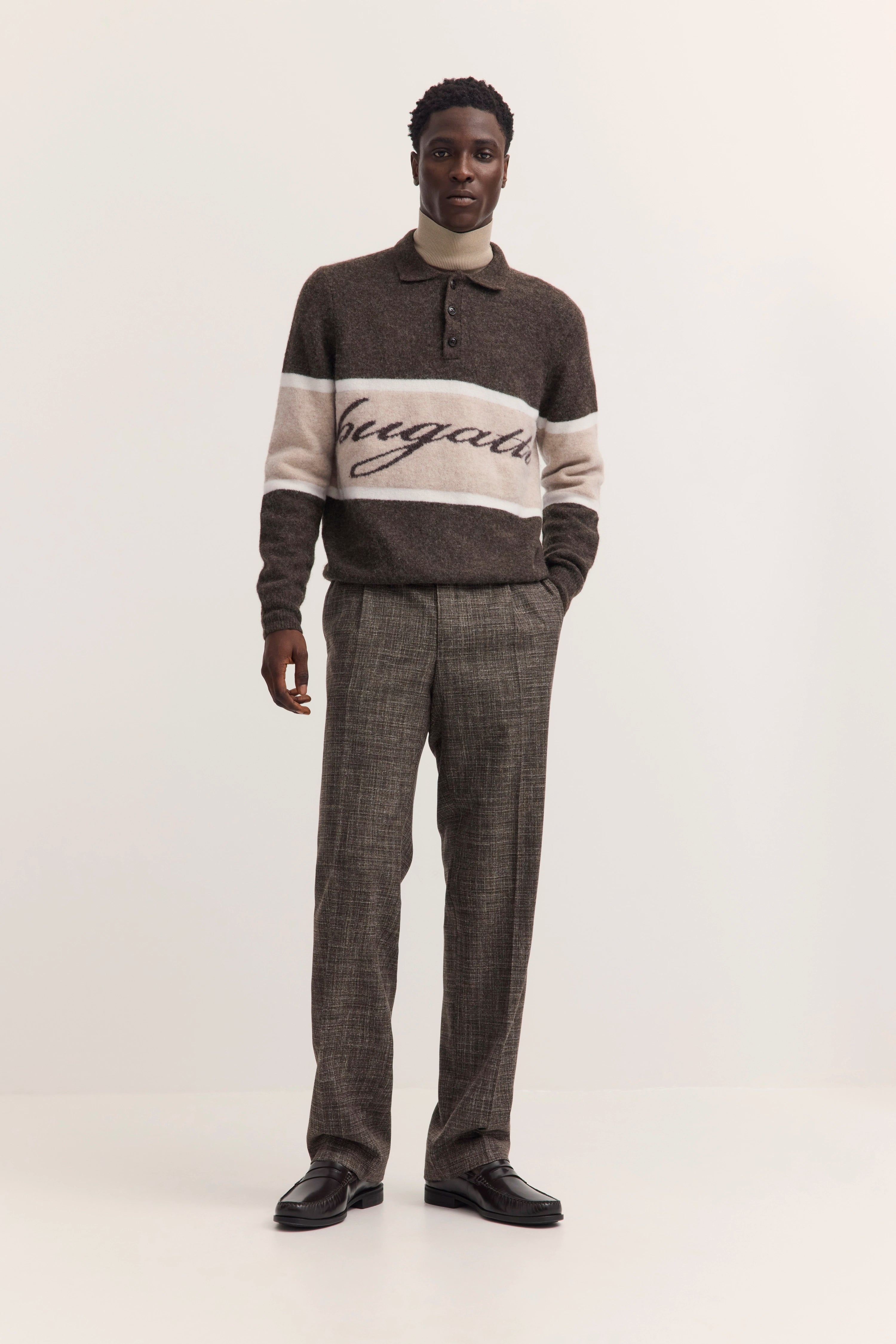 bugatti Pullover braun mit Logo, graue Hose, Modelbild stehend, lässige Pose.
