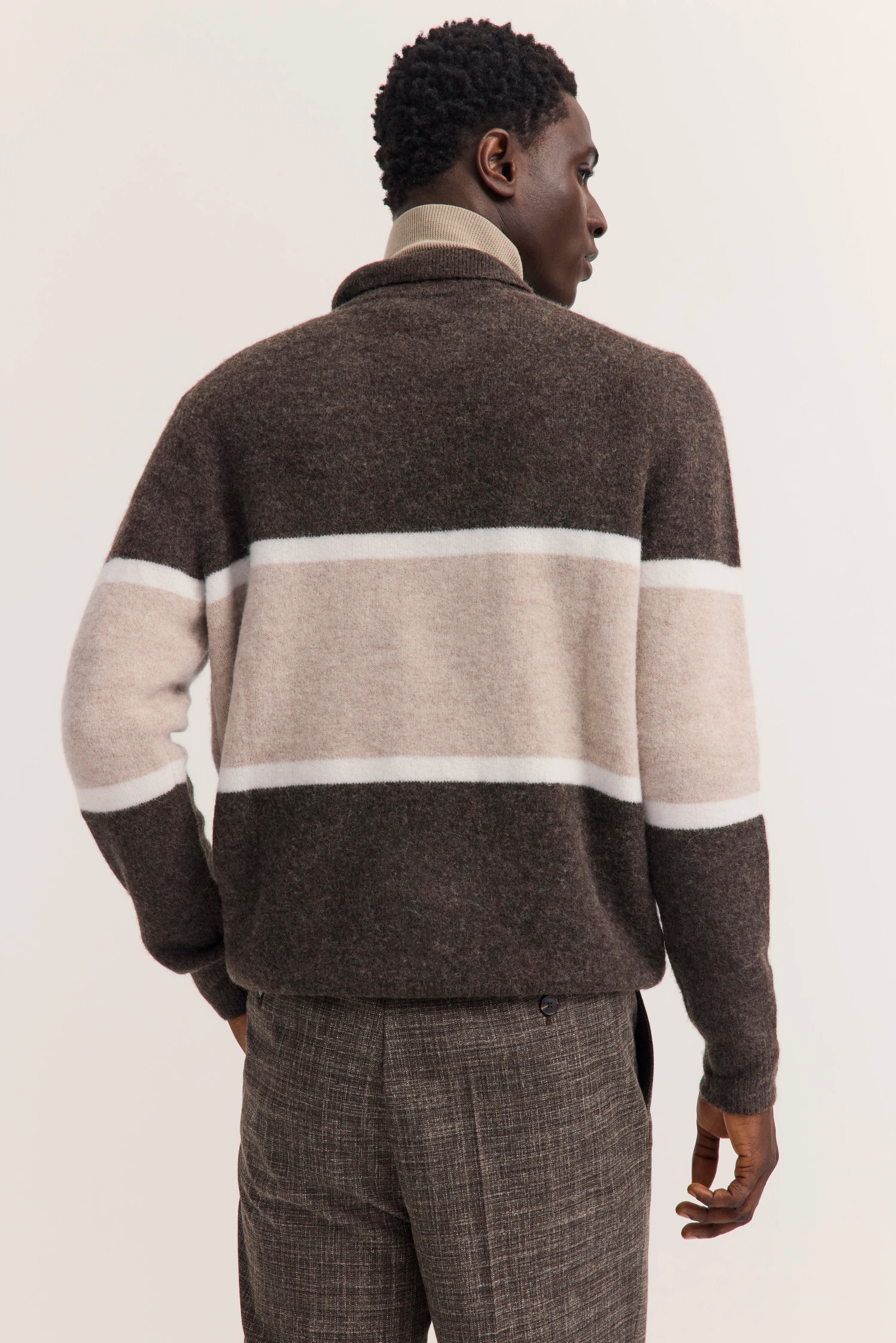 Brauner Pullover mit beige-weißen Streifen, Modell von hinten, lässige Hose in Braun, entspanntes Posing.