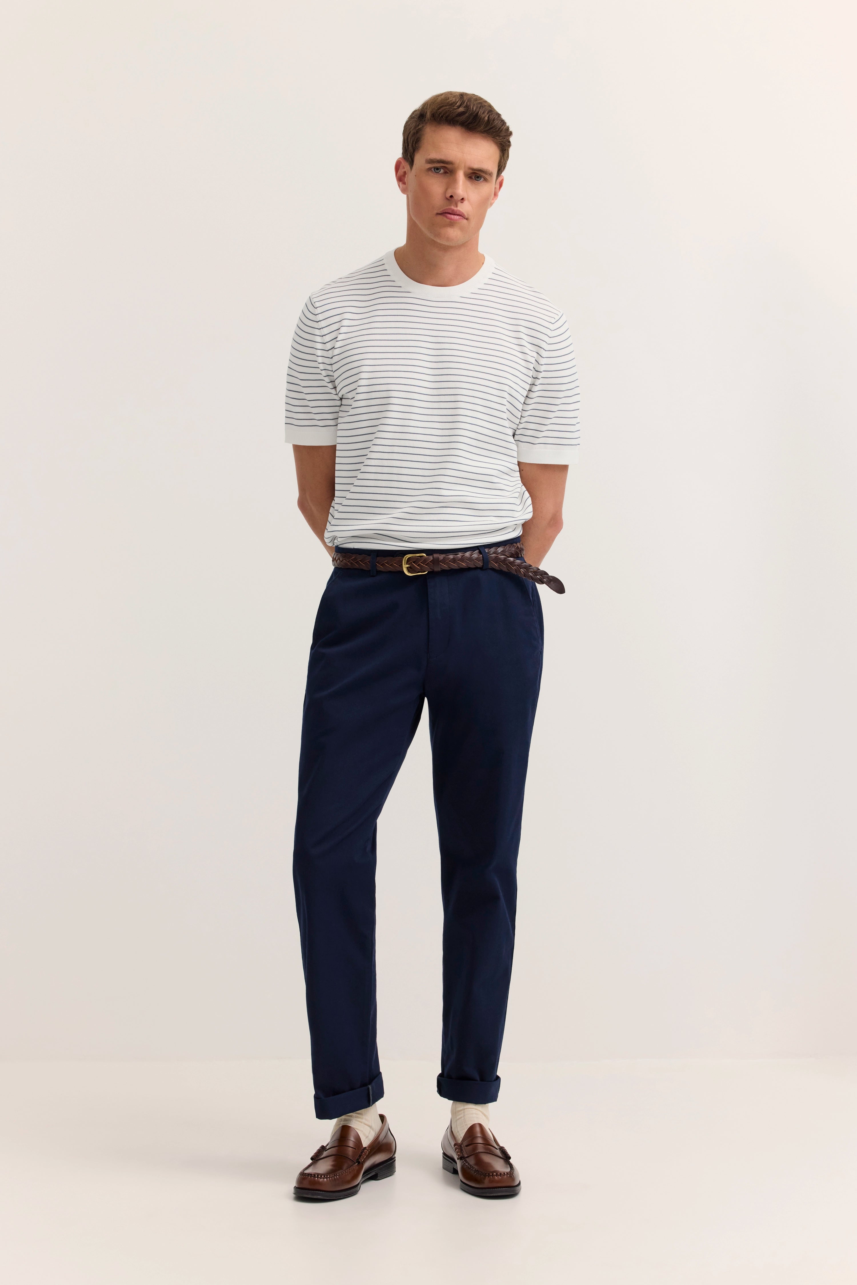 Bugatti Model mit weiß-blauem Streifen-Shirt, marineblauer Hose, braunen Loafers, entspannte Pose.
