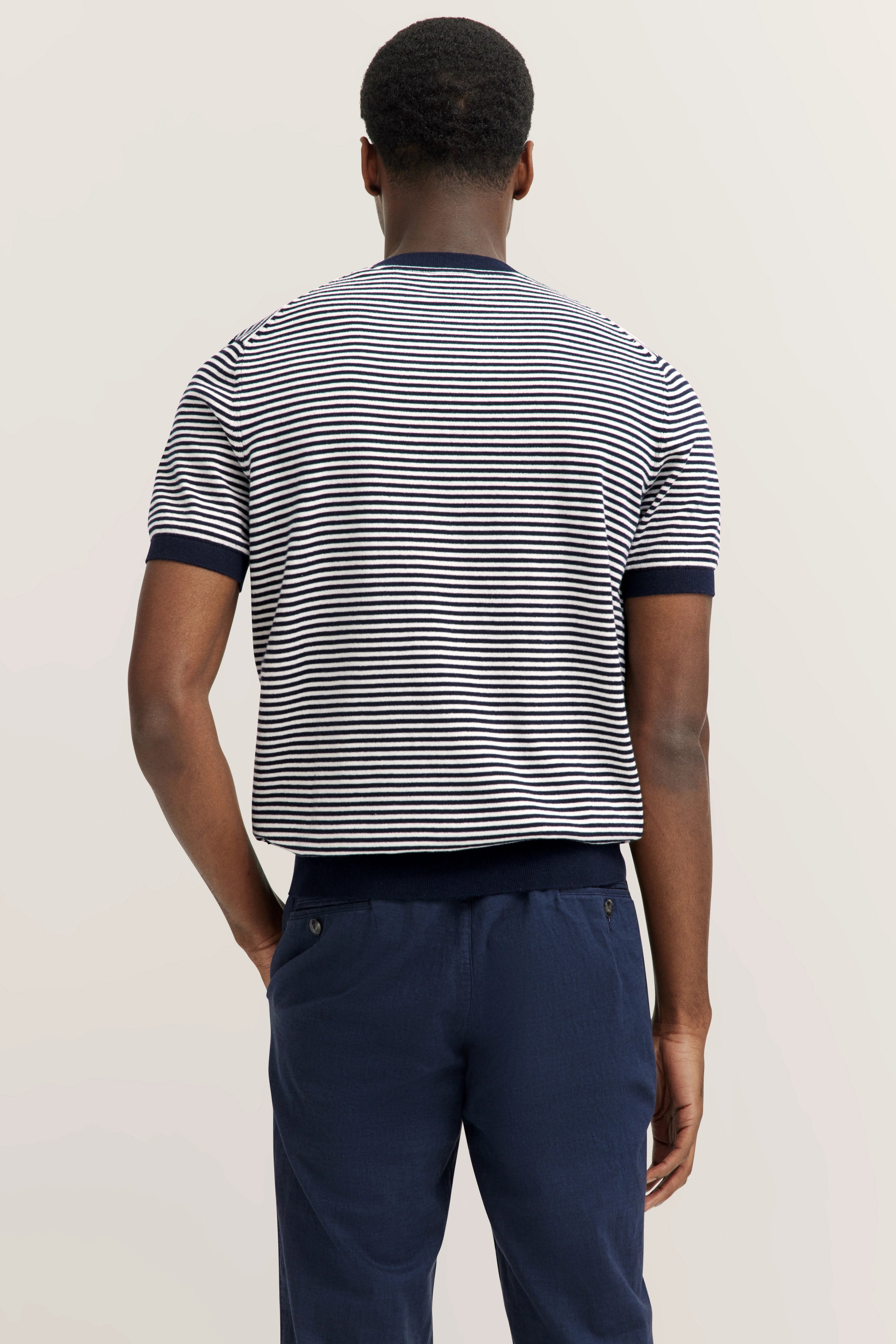 Gestreiftes T-Shirt in Weiß-Blau, dunkelblaue Hose, Modelbild von hinten.