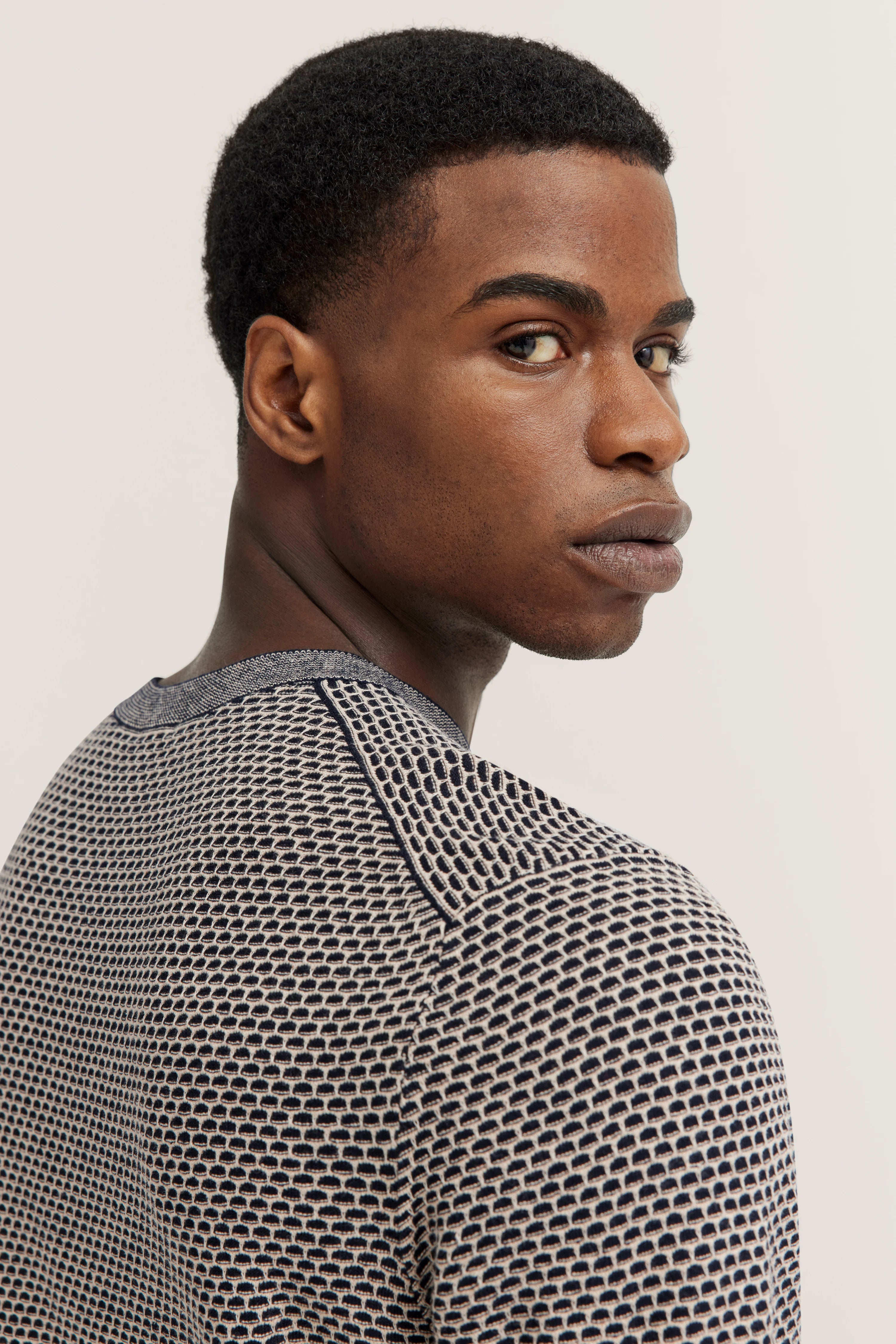 Model draagt bugatti trui in blauw-beige met geometrisch patroon, zijwaartse pose.