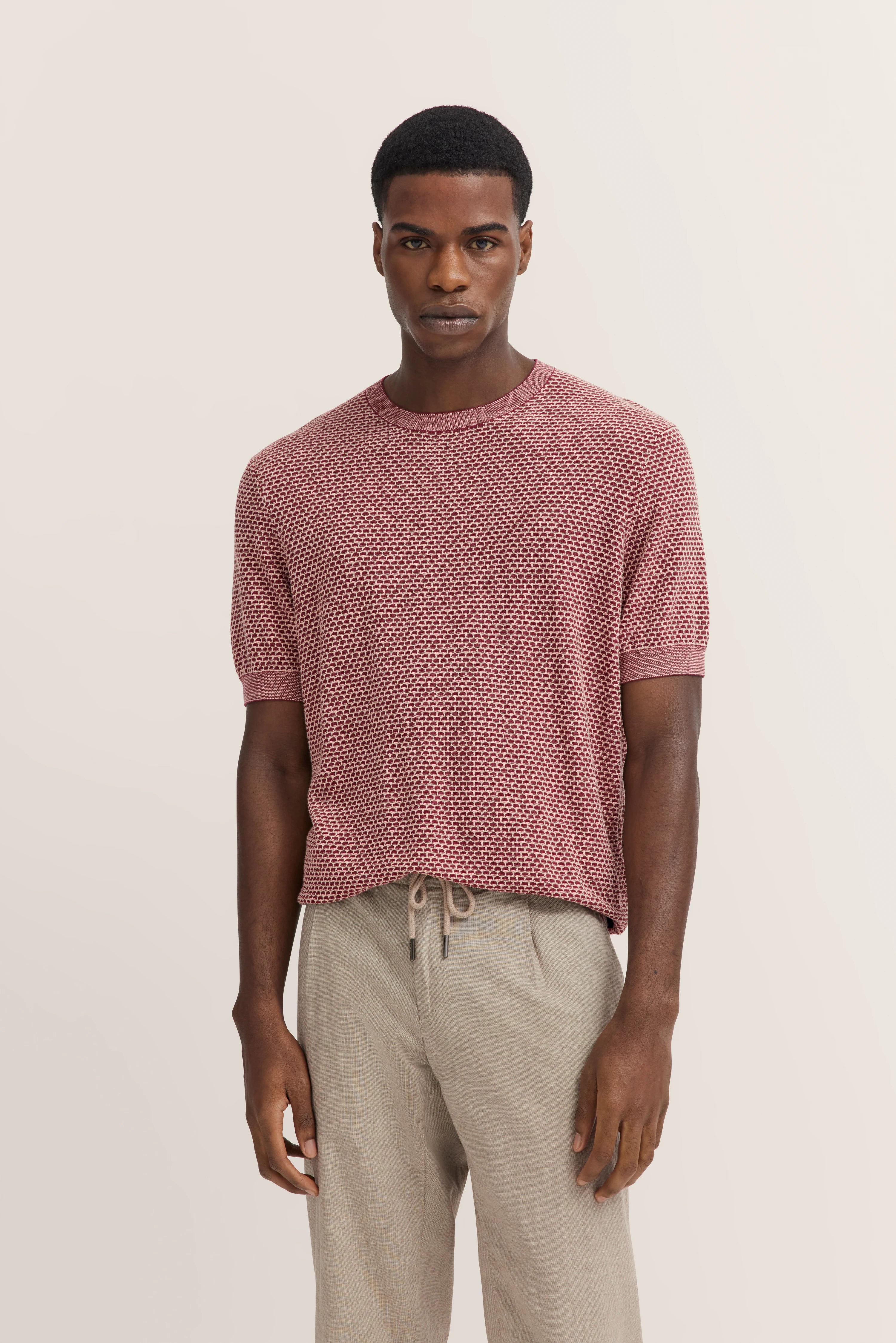 bugatti-model in rood patroon shirt en beige broek, ontspannen pose.