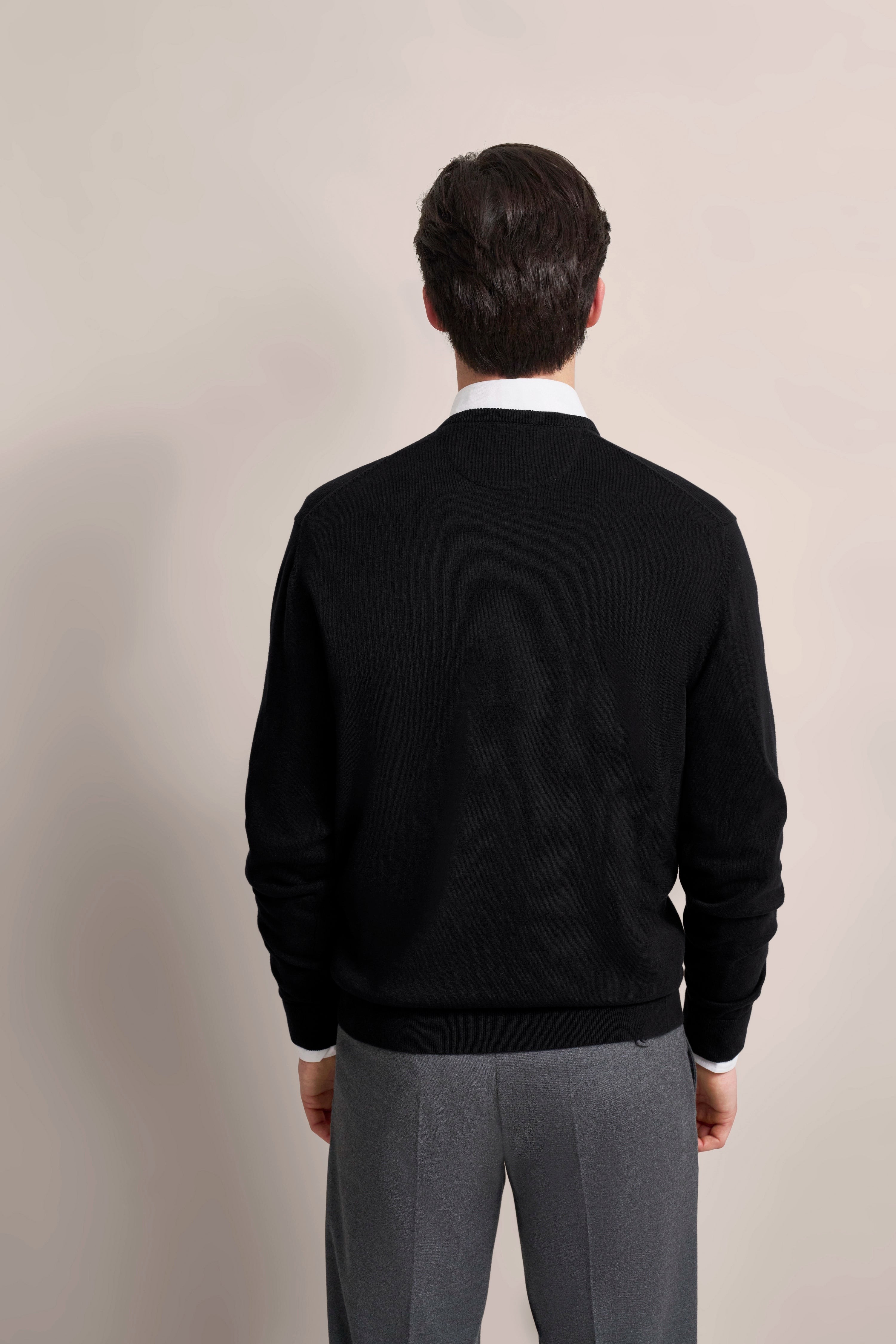 Rückansicht: Model in schwarzem bugatti Pullover, weißem Hemd, grauer Hose