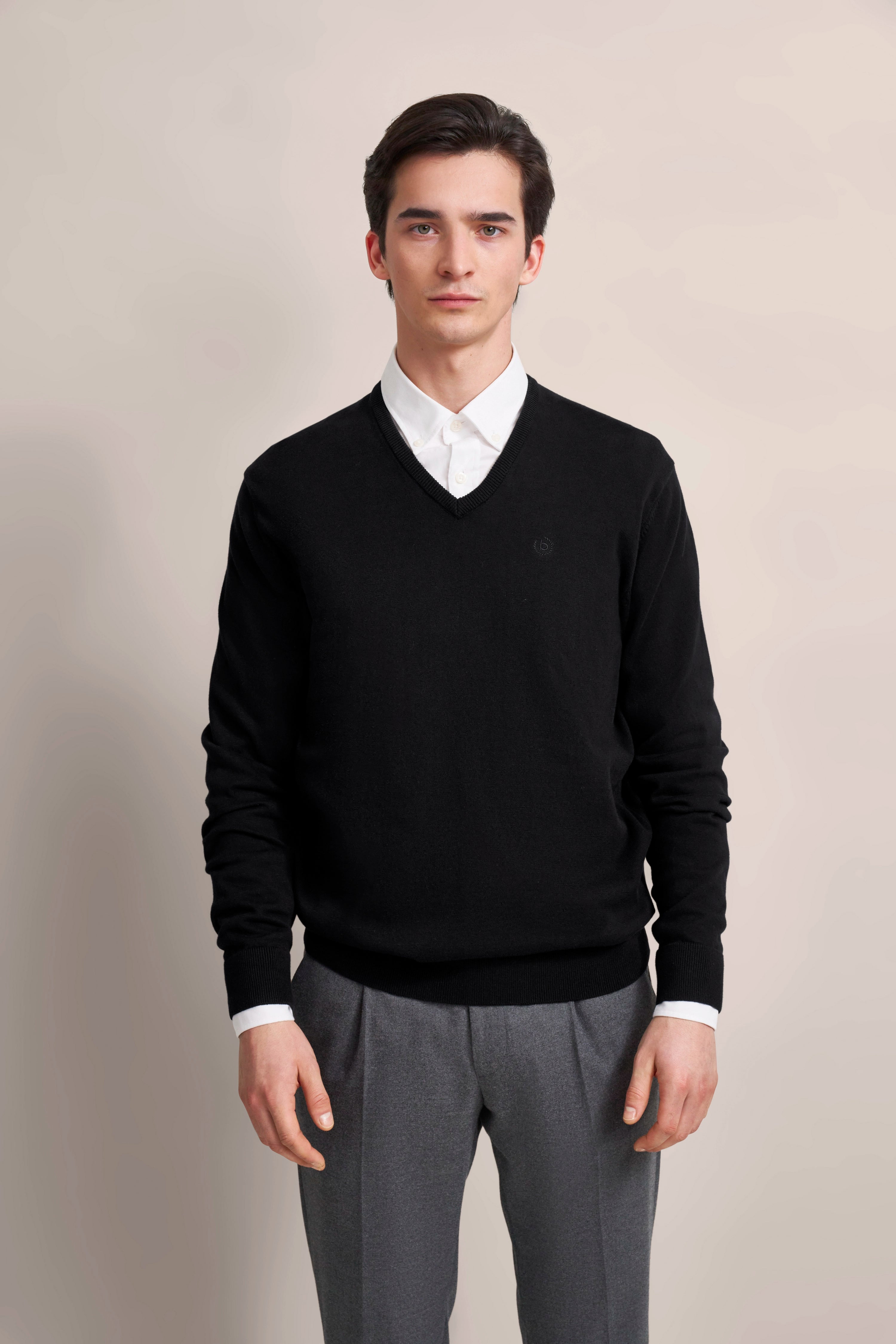 Elegant model in zwarte V-hals trui en wit shirt van bugatti, grijze broek.