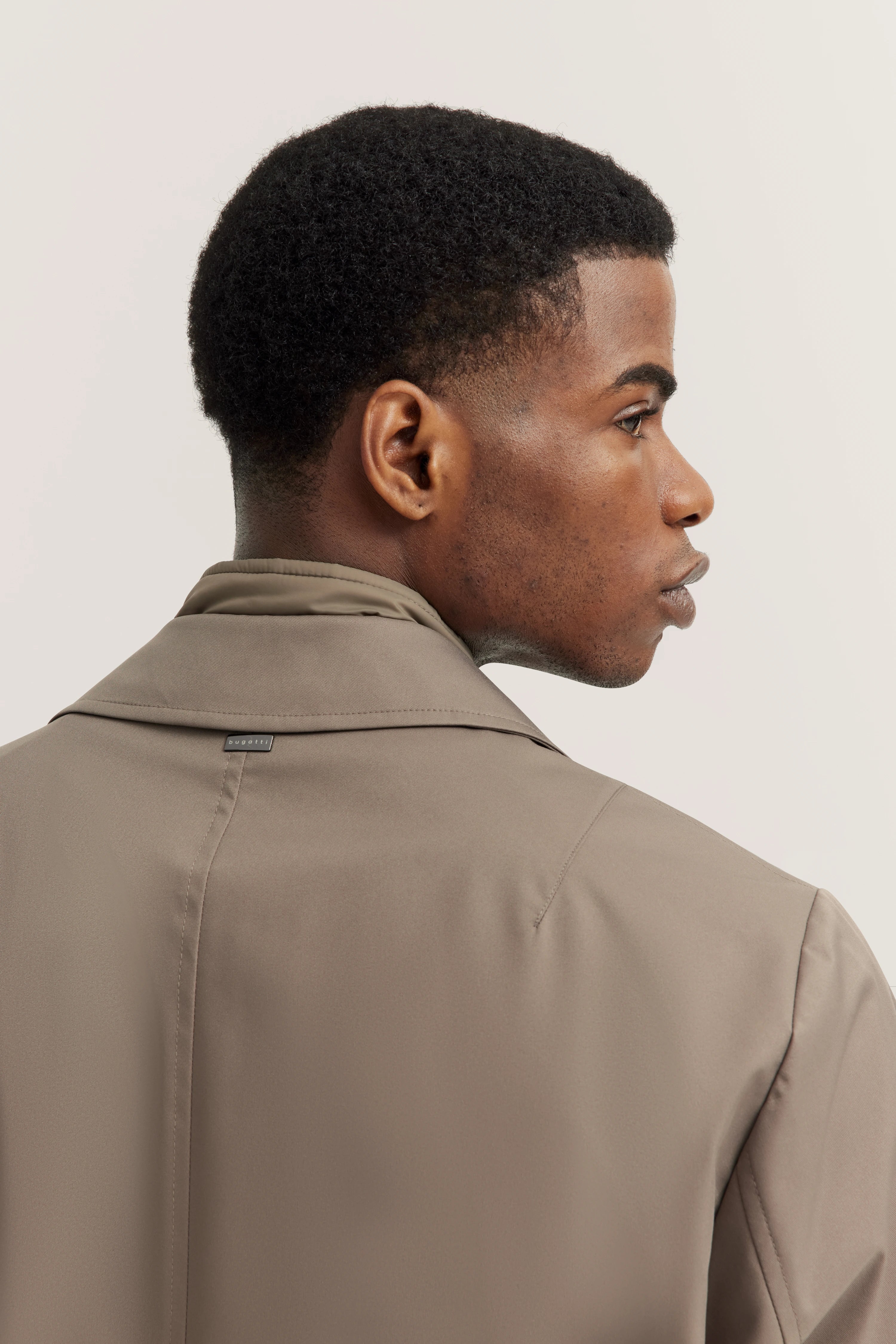 bugatti Trenchcoat in Taupe, Modelbild von hinten, Kopf seitlich gedreht, elegant und zeitlos.