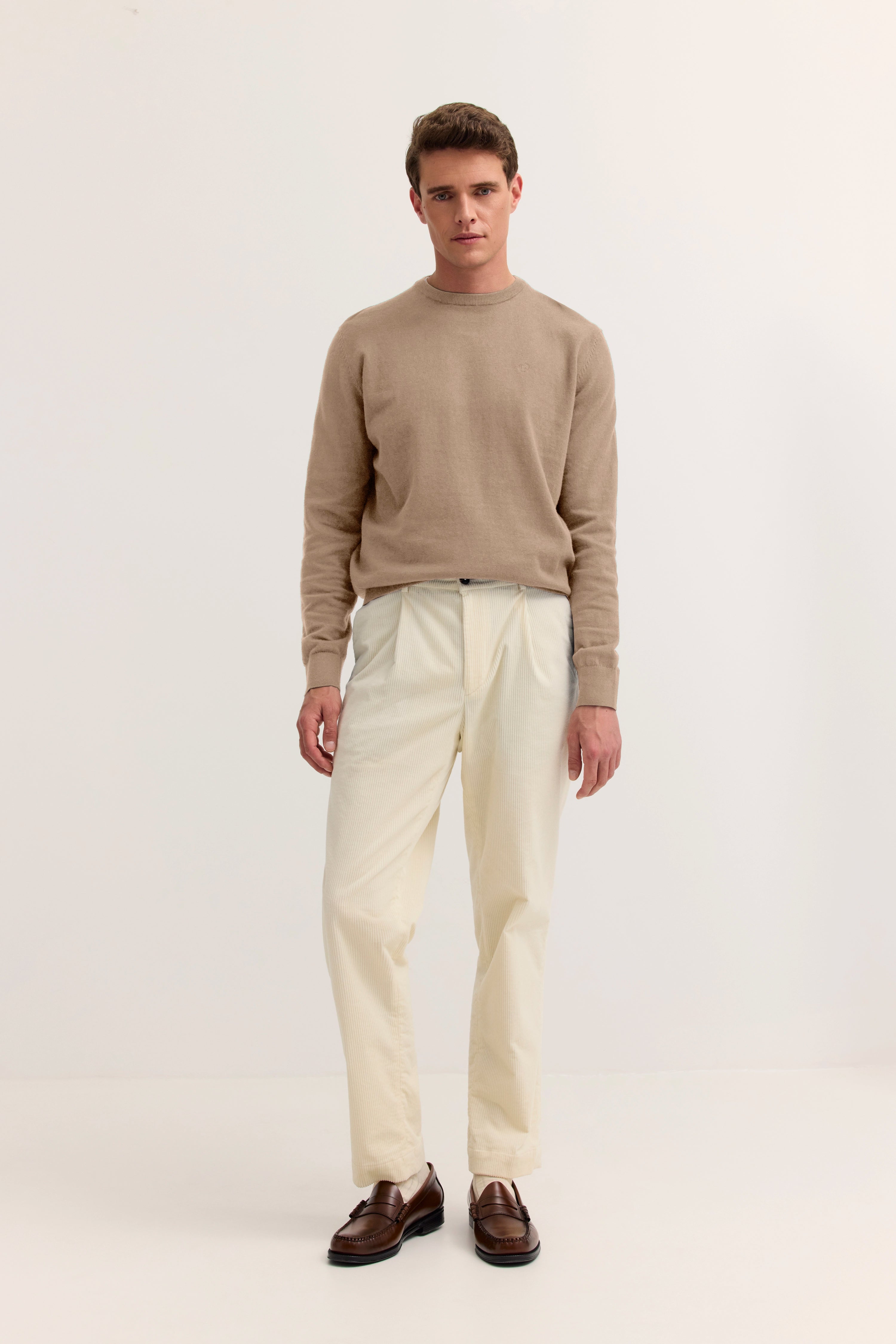 Beiger Pullover und cremefarbene Hose, braune Schuhe, Model in entspannter Haltung.