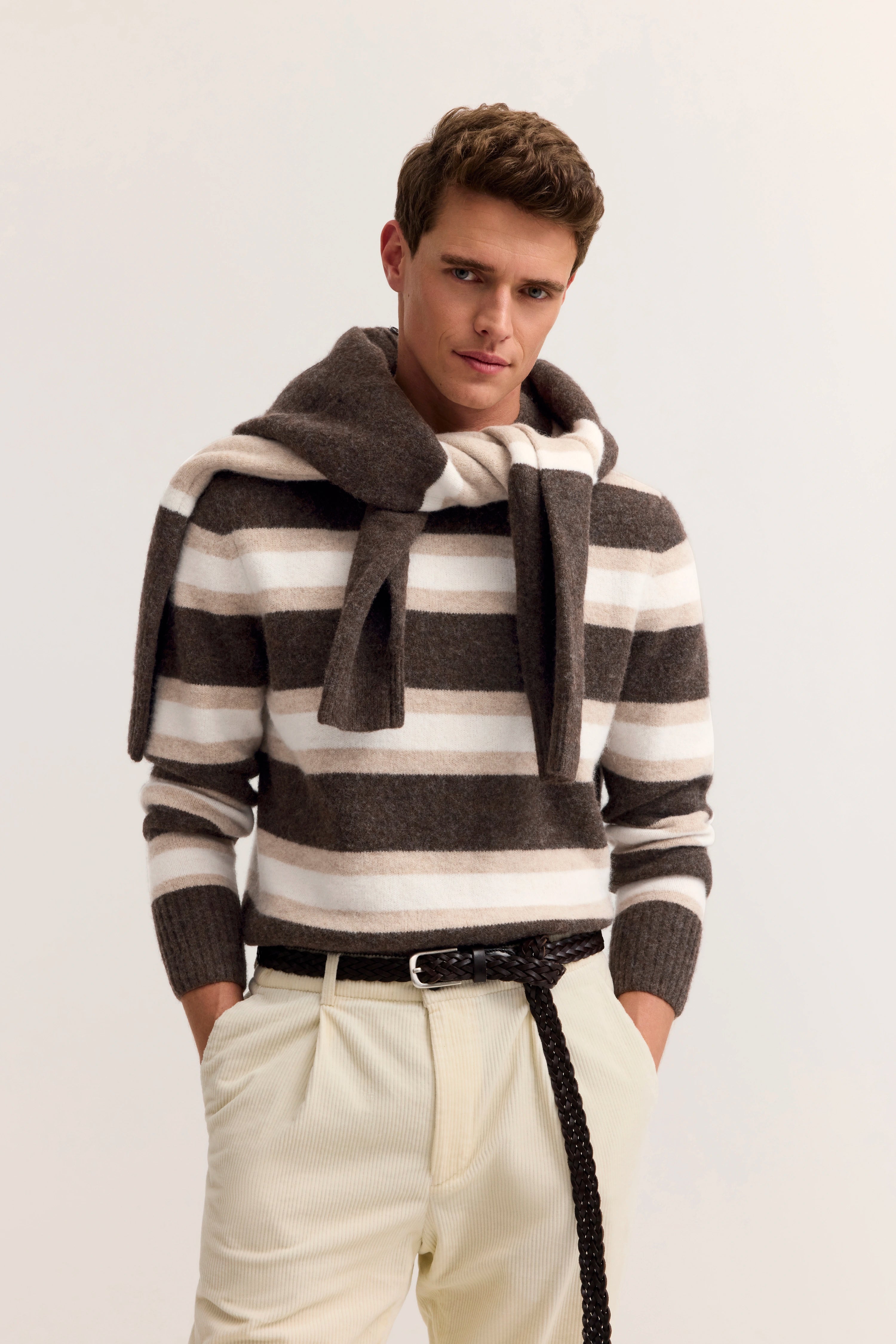 "bugatti Modelbild: Mann in gestreiftem Pullover in Braun und Beige, legeres Posing mit Händen in Taschen."