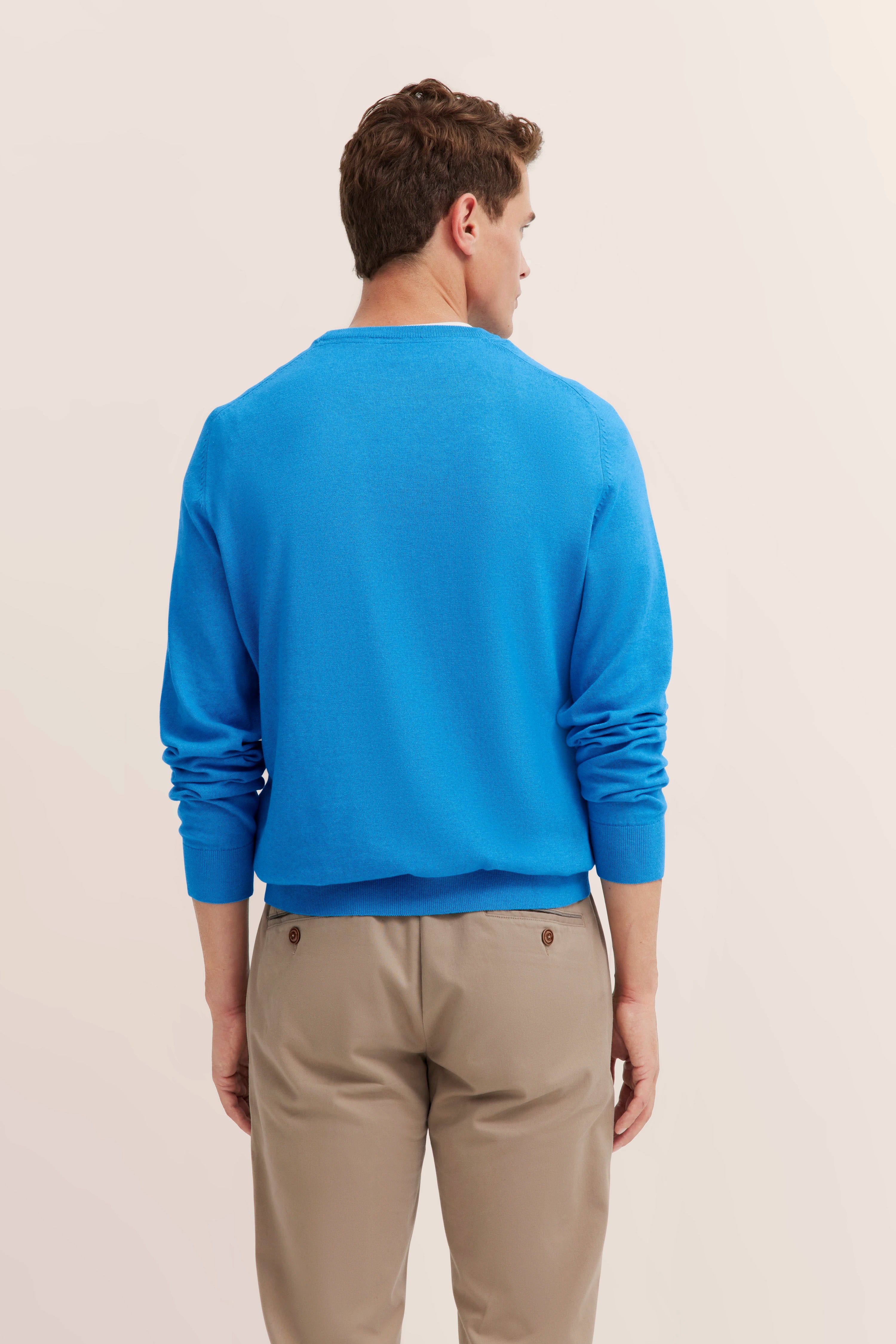 Blue bugatti sweater, beige pants, model from behind, casual pose.