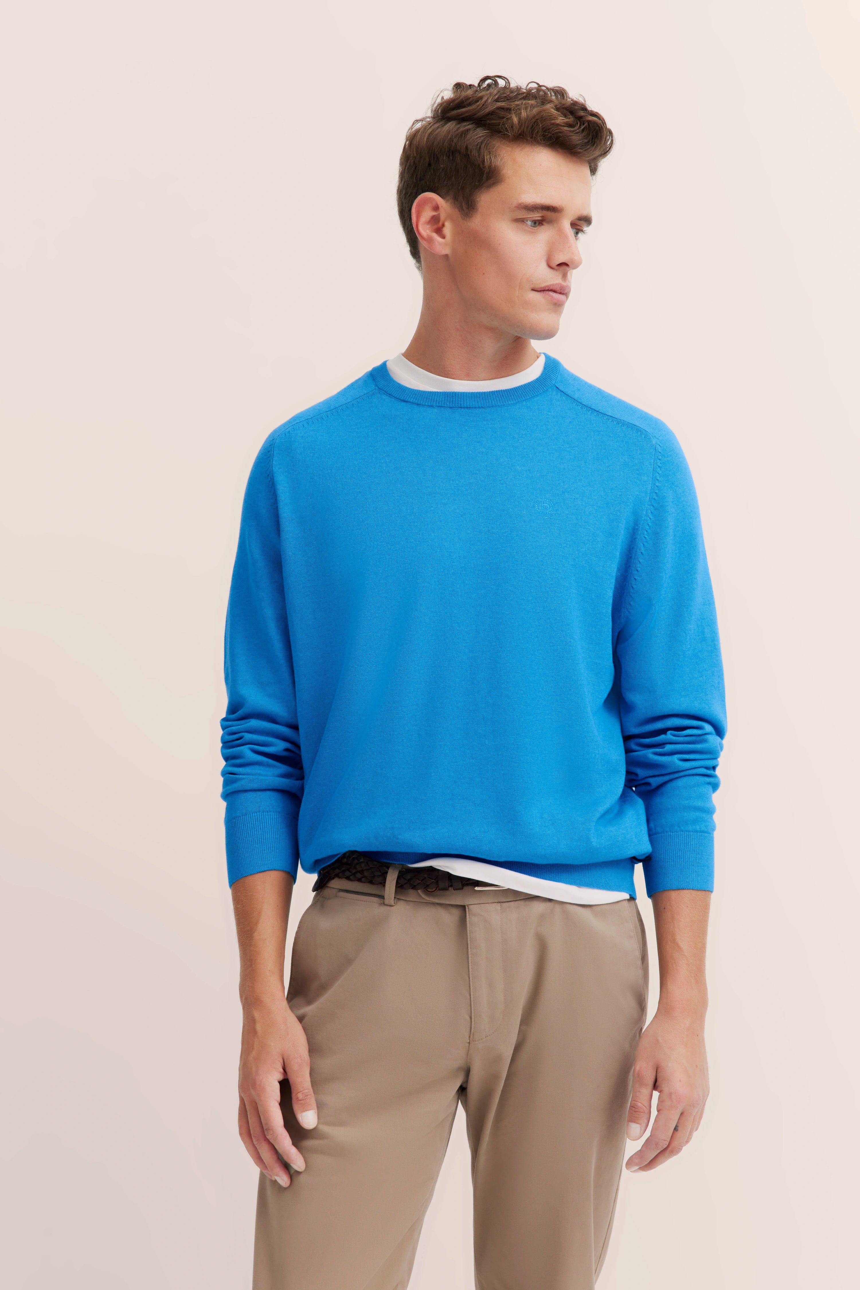 bugatti model in blue sweater and beige pants, standing sideways.