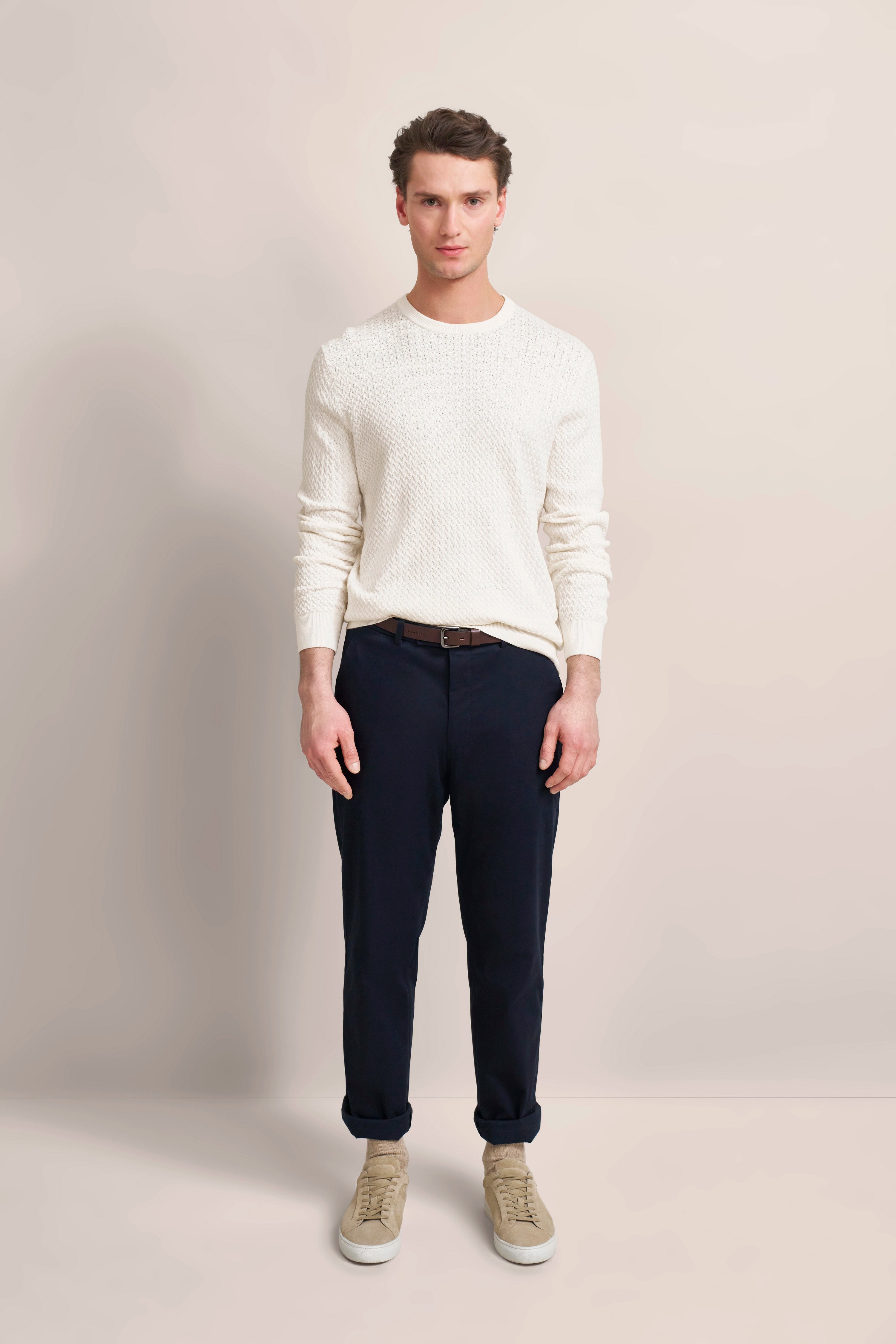 White knit sweater with dark blue trousers, model facing front, beige sneakers, embodying bugatti's refined elegance.