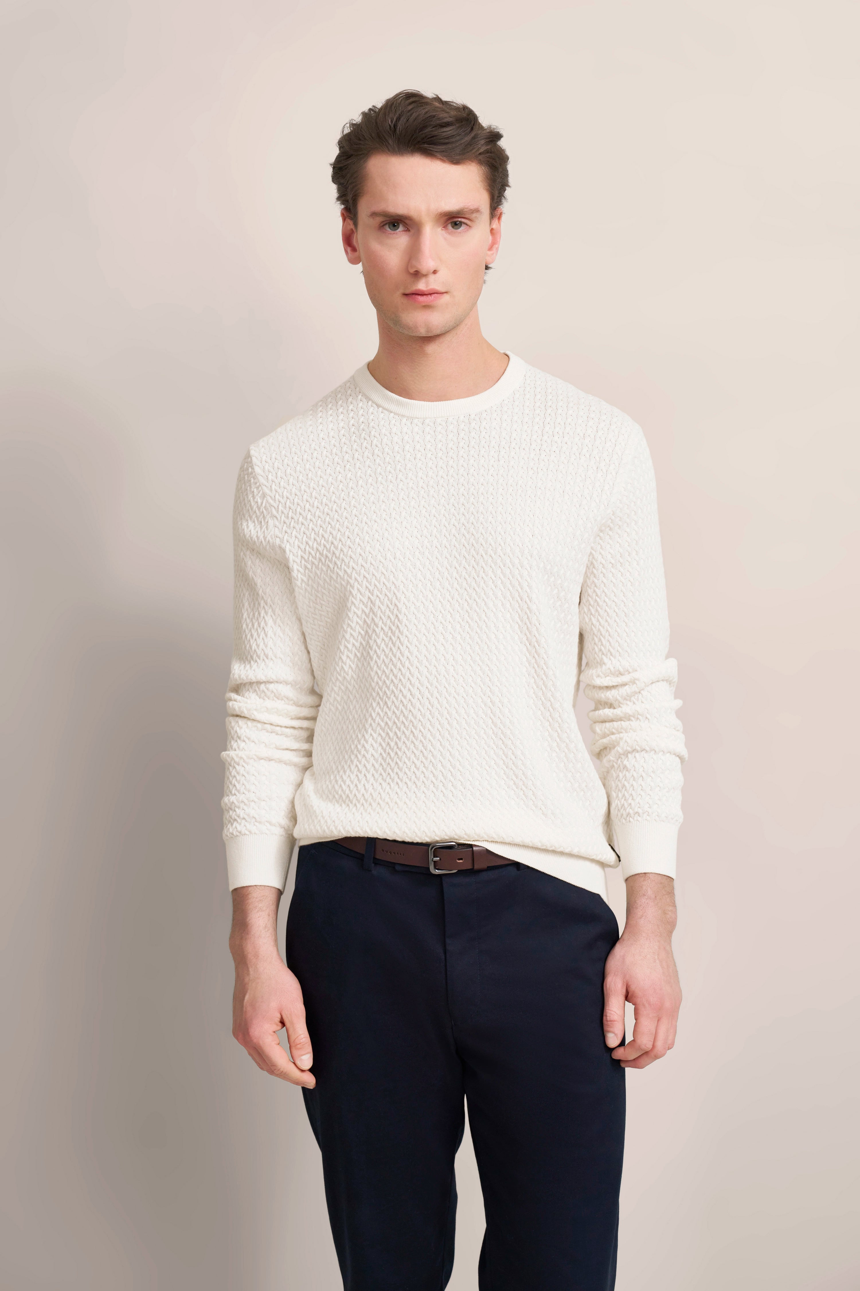White knit sweater and dark blue pants, model standing relaxed.