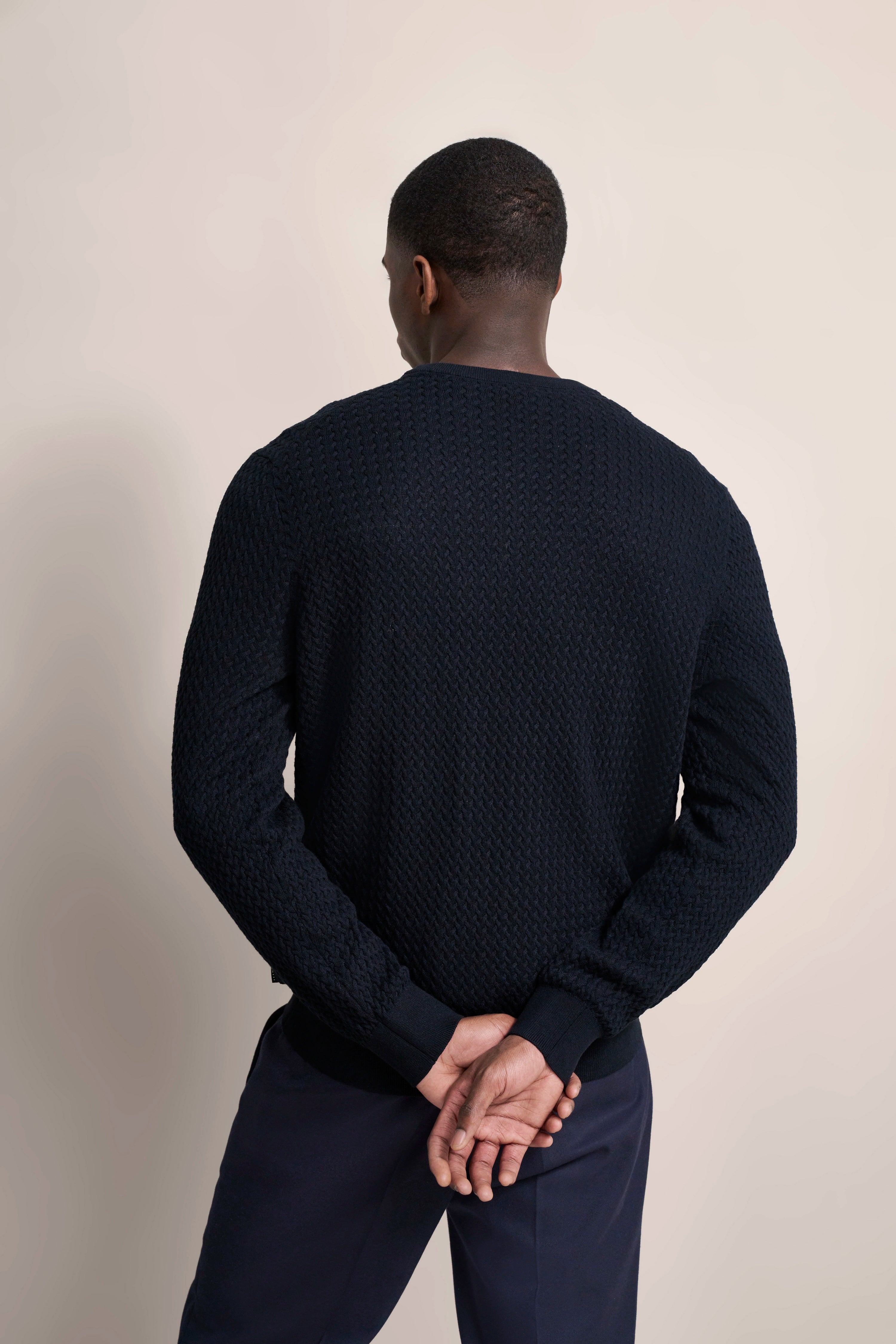 Rückenansicht: Model trägt einen dunkelblauen Strickpullover, Arme verschränkt, lässiges Posen.
