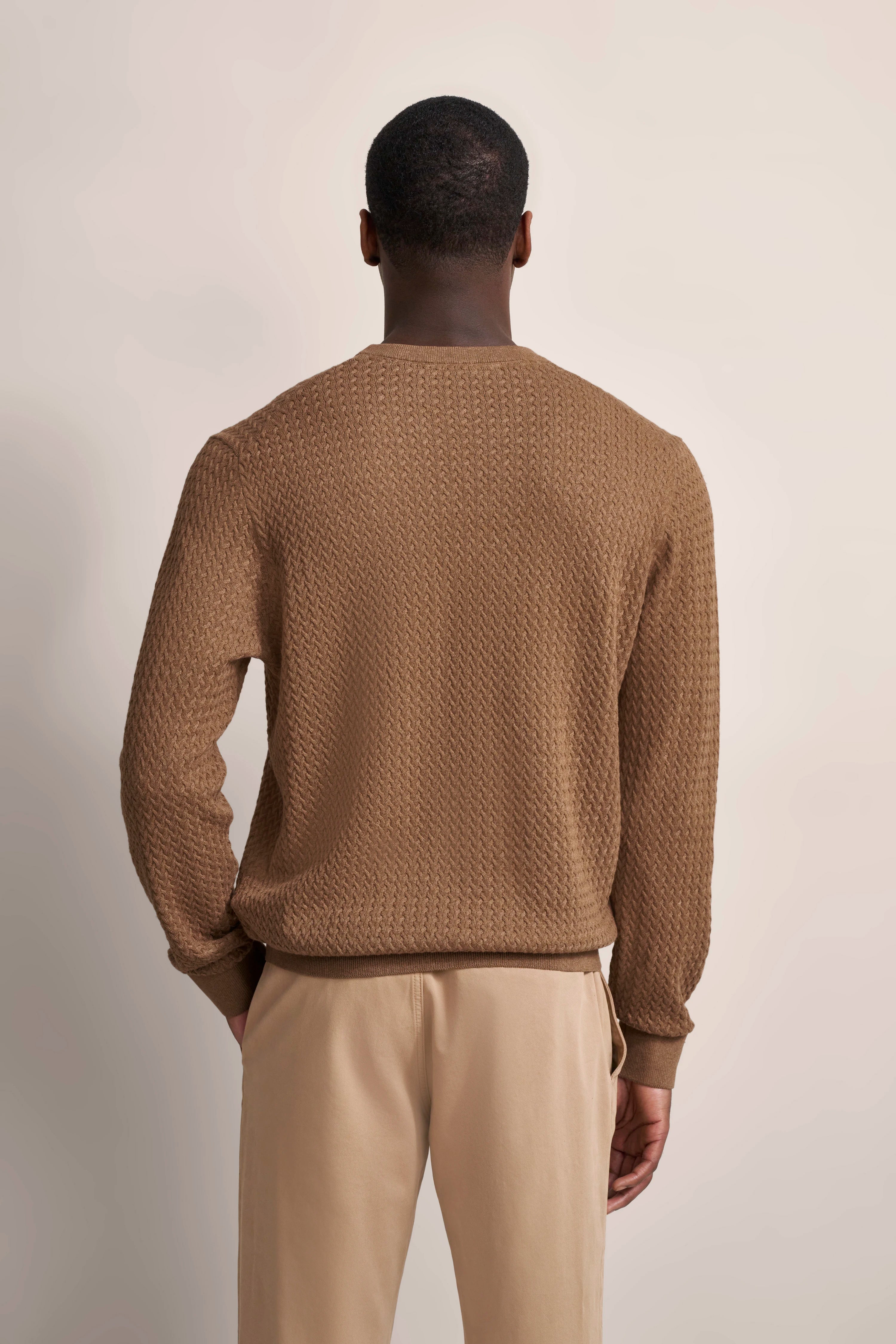 Brauner Strickpullover mit Muster, beige Hose, Model von hinten, legeres Posing.