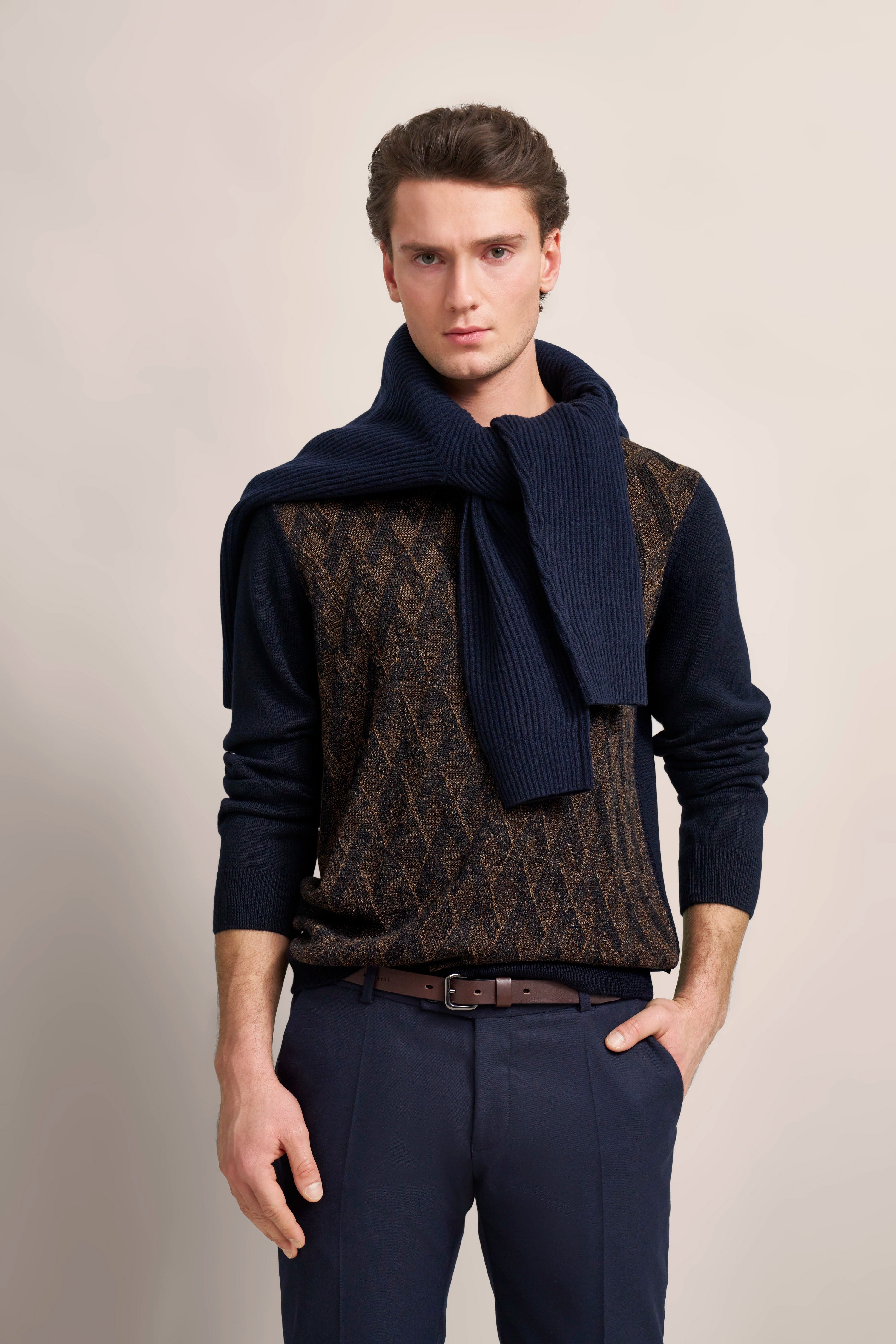 Modelbild: Mann im braun-blau gemusterten Pullover mit navy Schal von bugatti, Posen mit Hand in der Tasche.