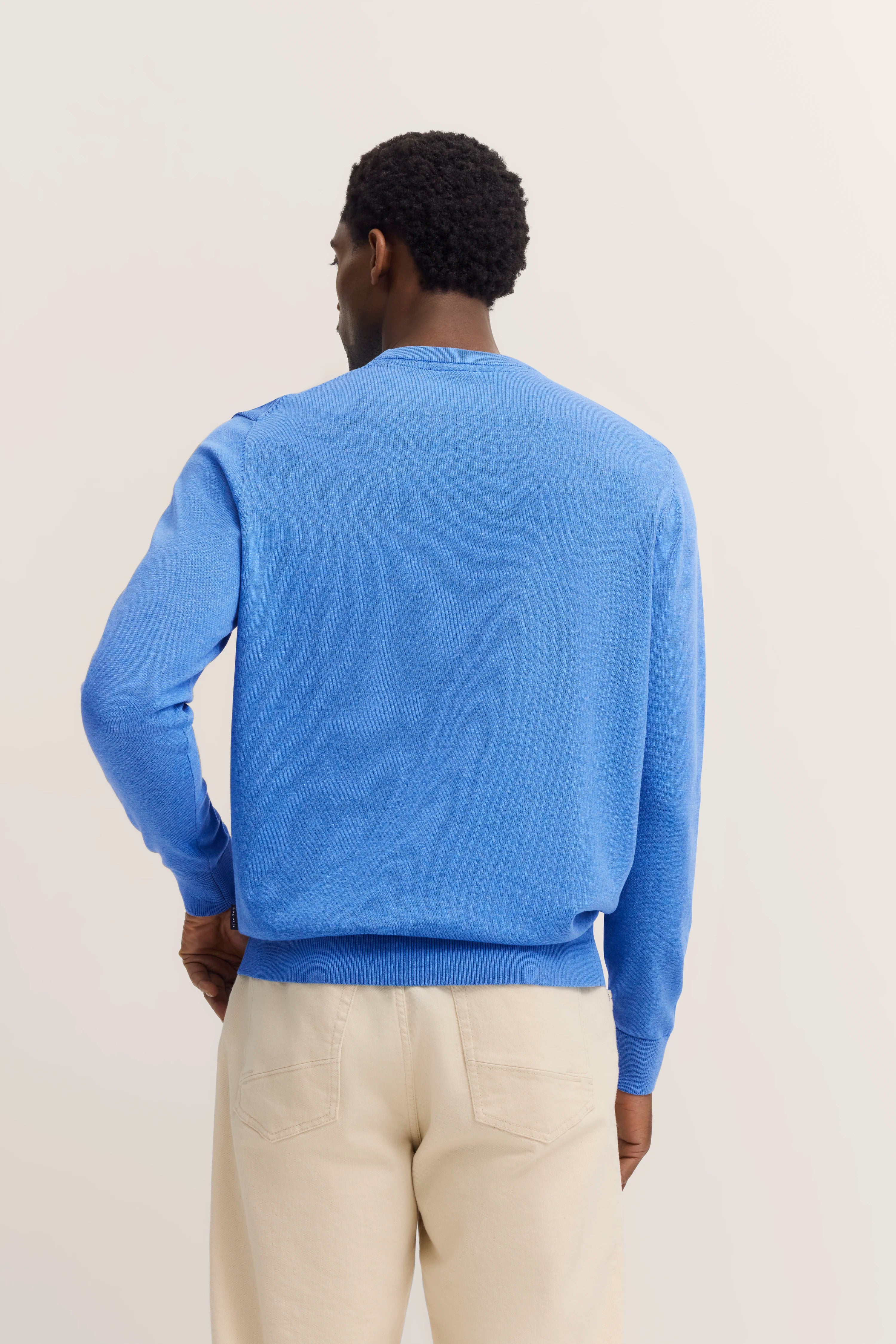 Blauwe bugatti trui, achterkant, crèmekleurige broek, casual model, ontspannen houding.