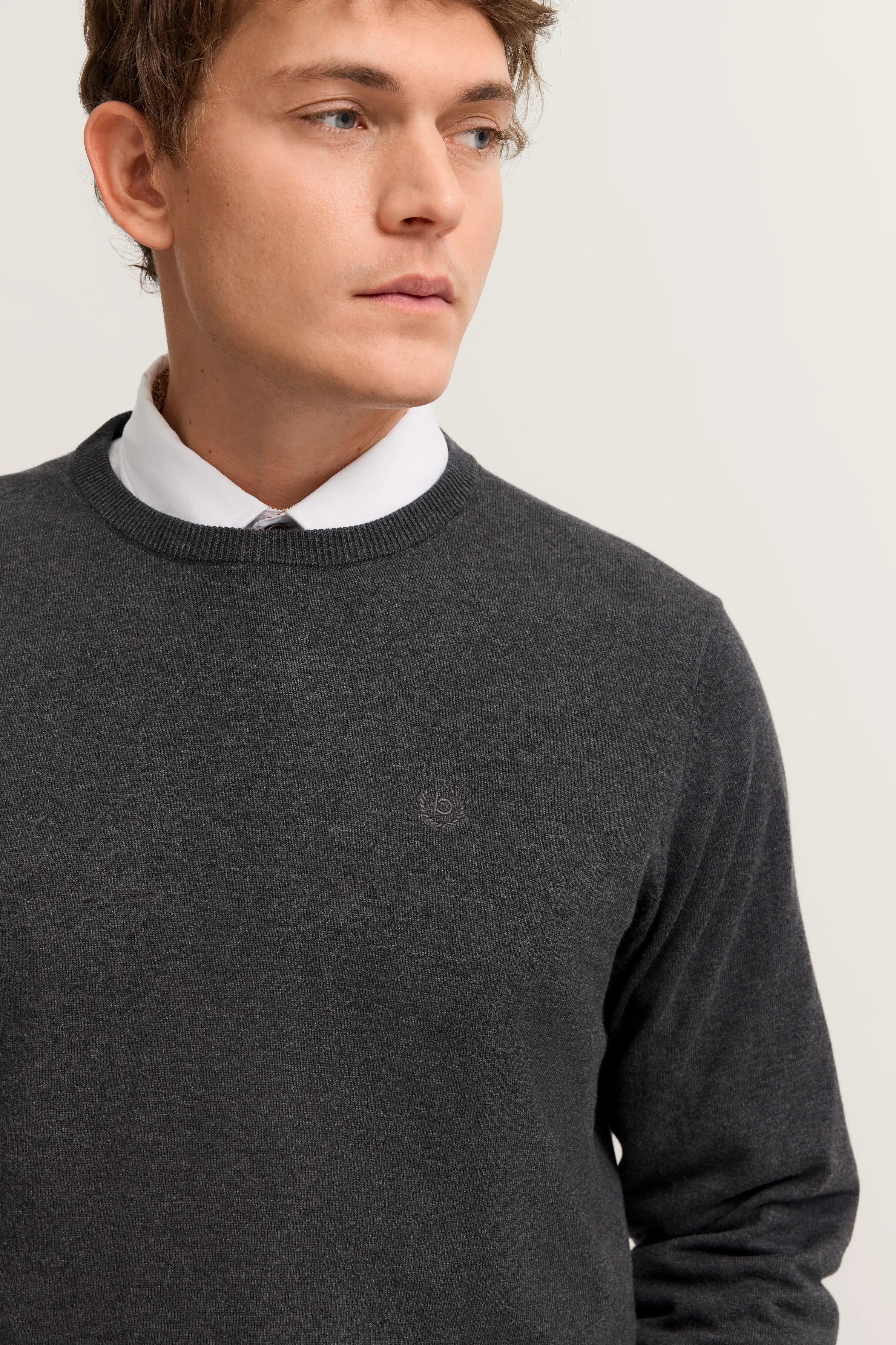 Grauer bugatti Pullover über weißem Hemd, legeres Modelbild mit Blick zur Seite.