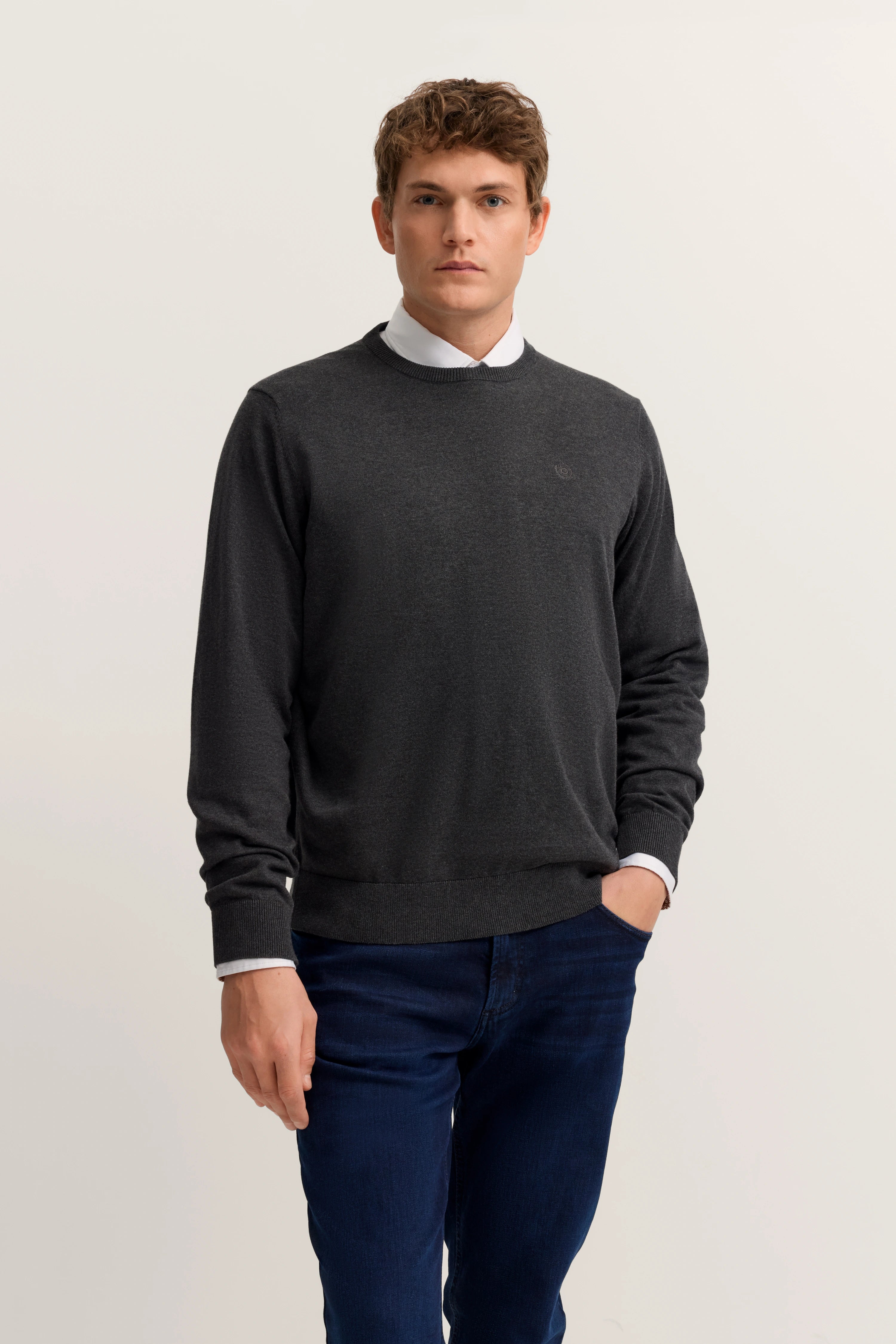 Model in dunklem Pullover und blauer Jeans, Hände in Taschen, lässige Pose.