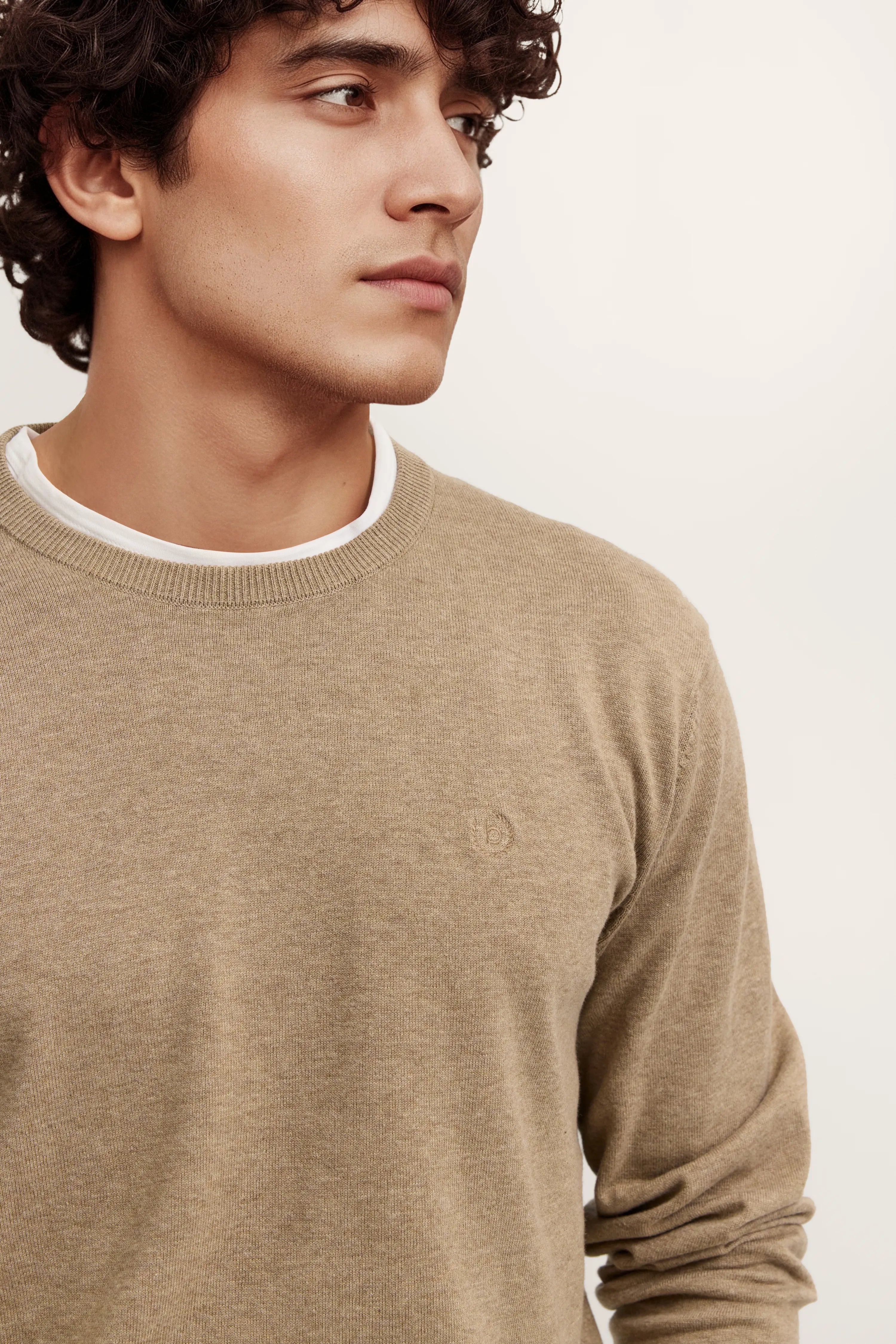 Bugatti Pullover beige, legeres Modelbild, entspannte Pose, weiße Unterlage sichtbar.