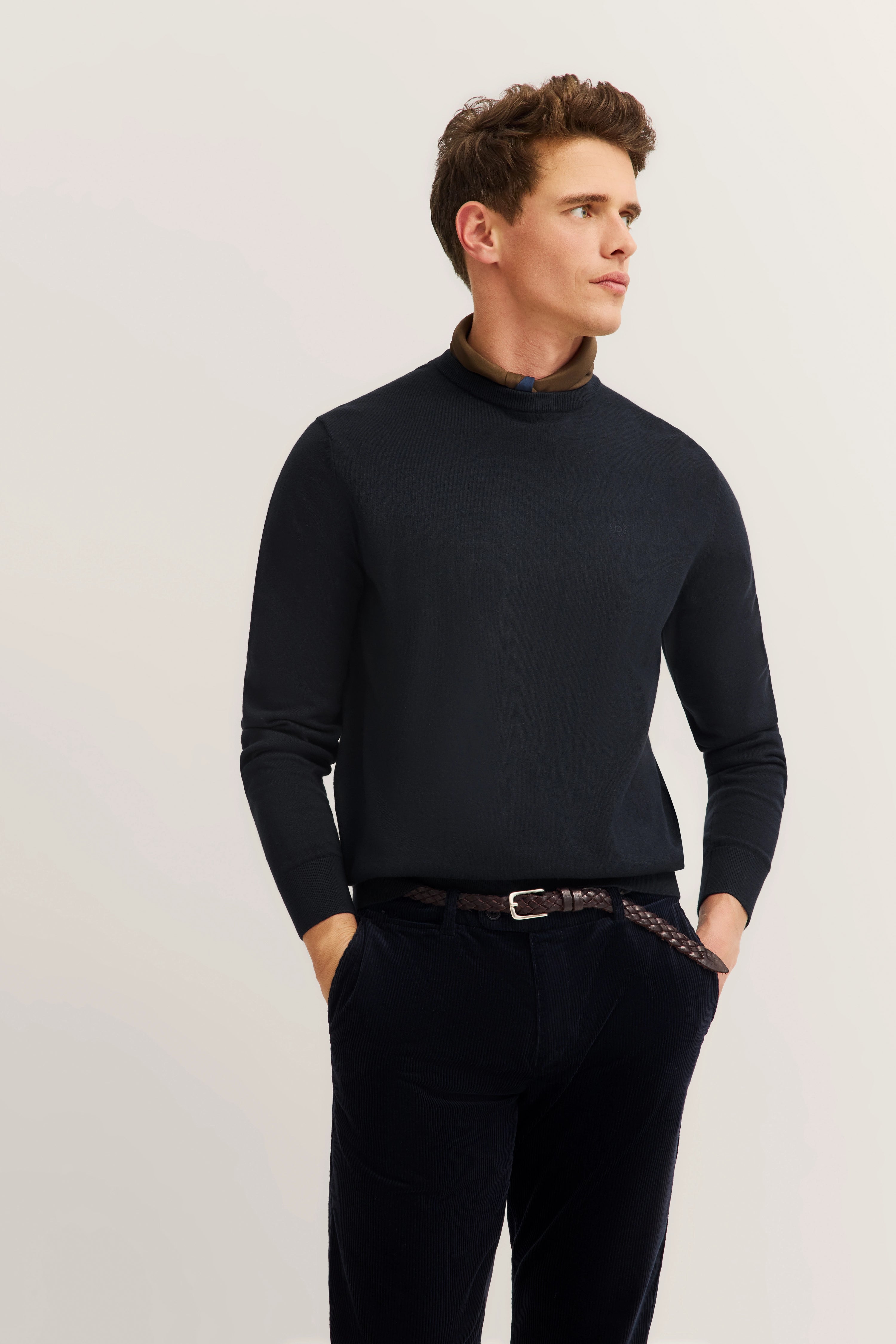 bugatti Modelbild, schwarzer Pullover, brauner Kragen, brauner Gürtel, lässige Pose, seitlicher Blick.