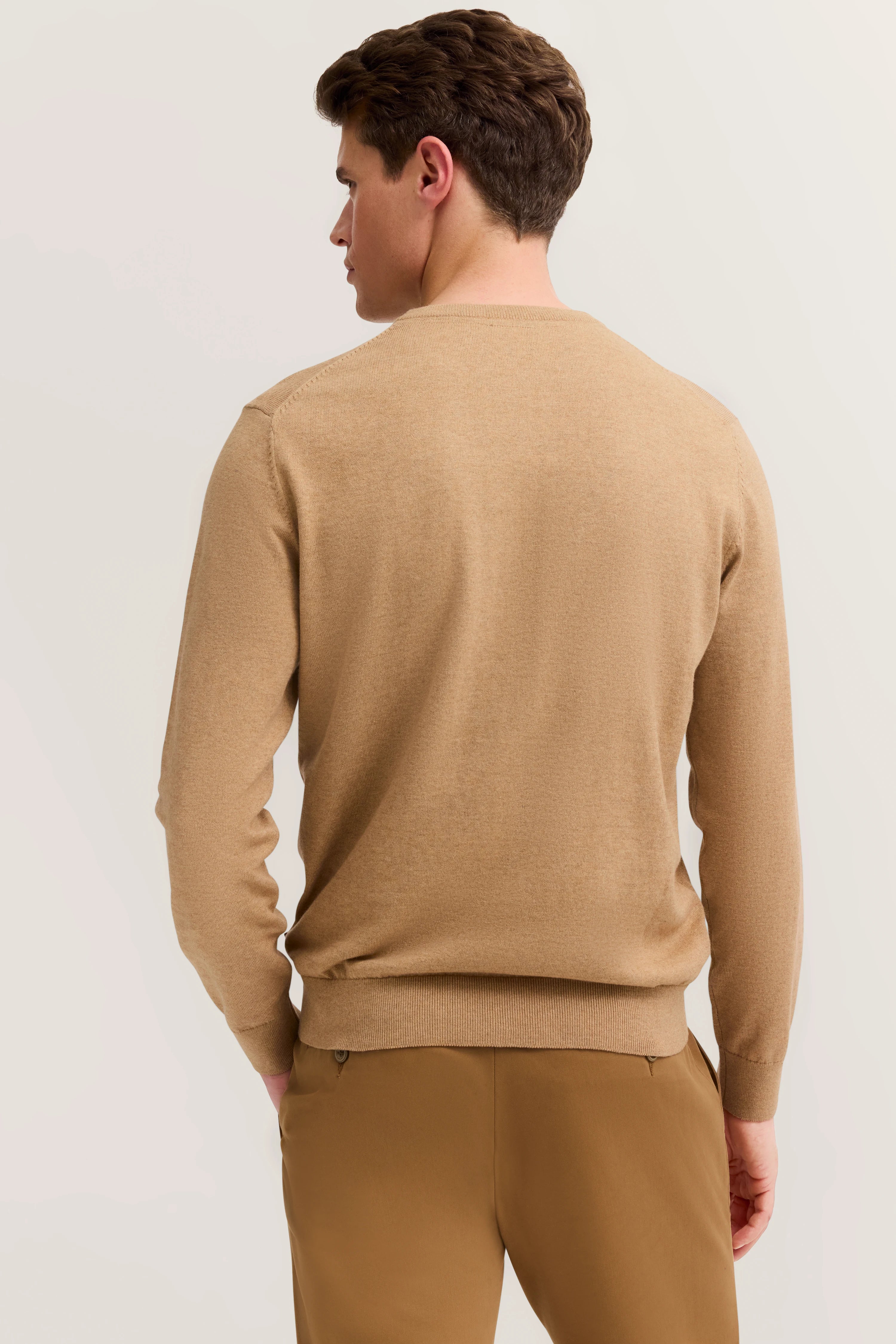 Bugatti Modelbild, beige Pullover und Hose, Rückansicht, entspannte Pose.