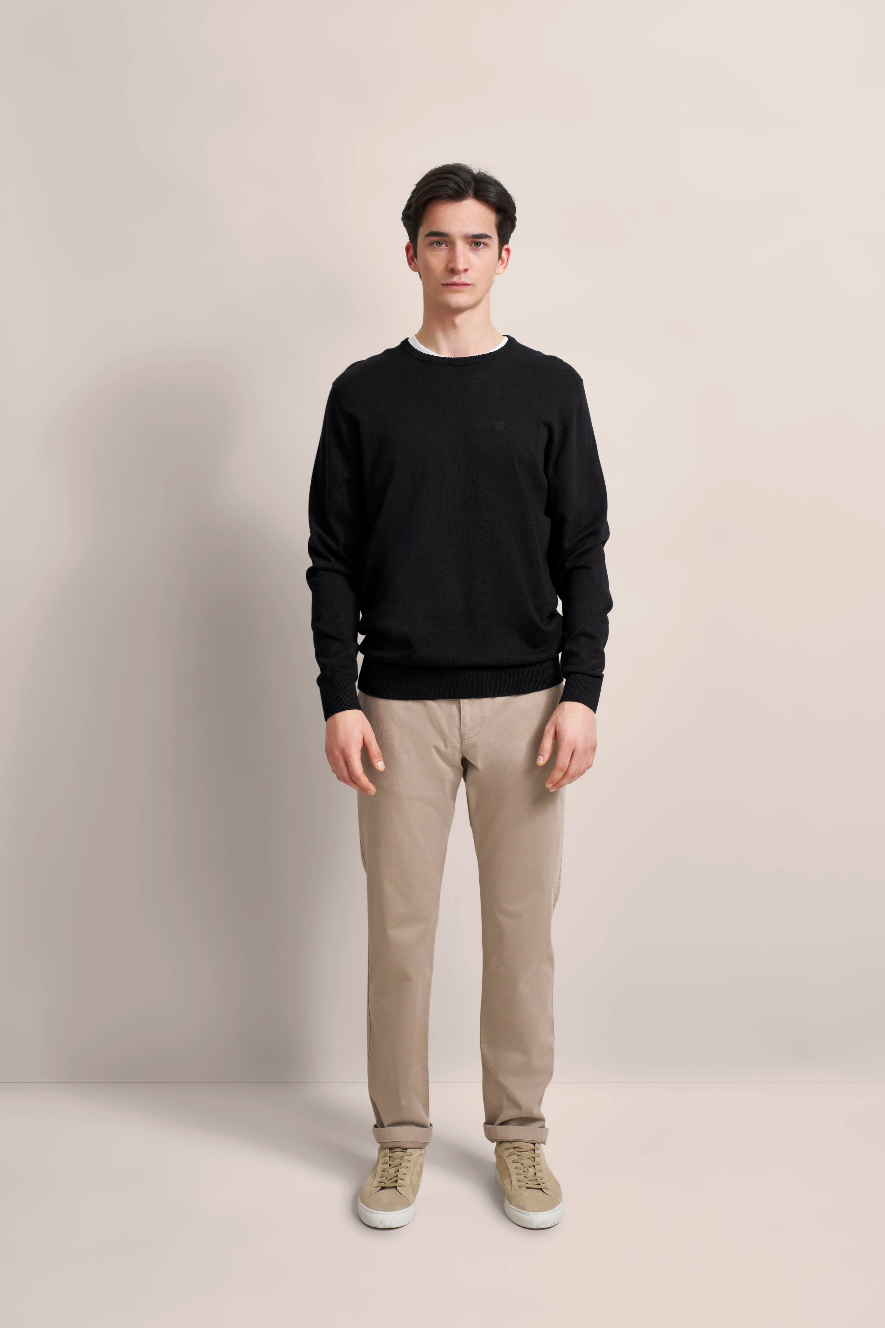 Model in schwarzem Pullover und beiger Hose, frontal stehend.