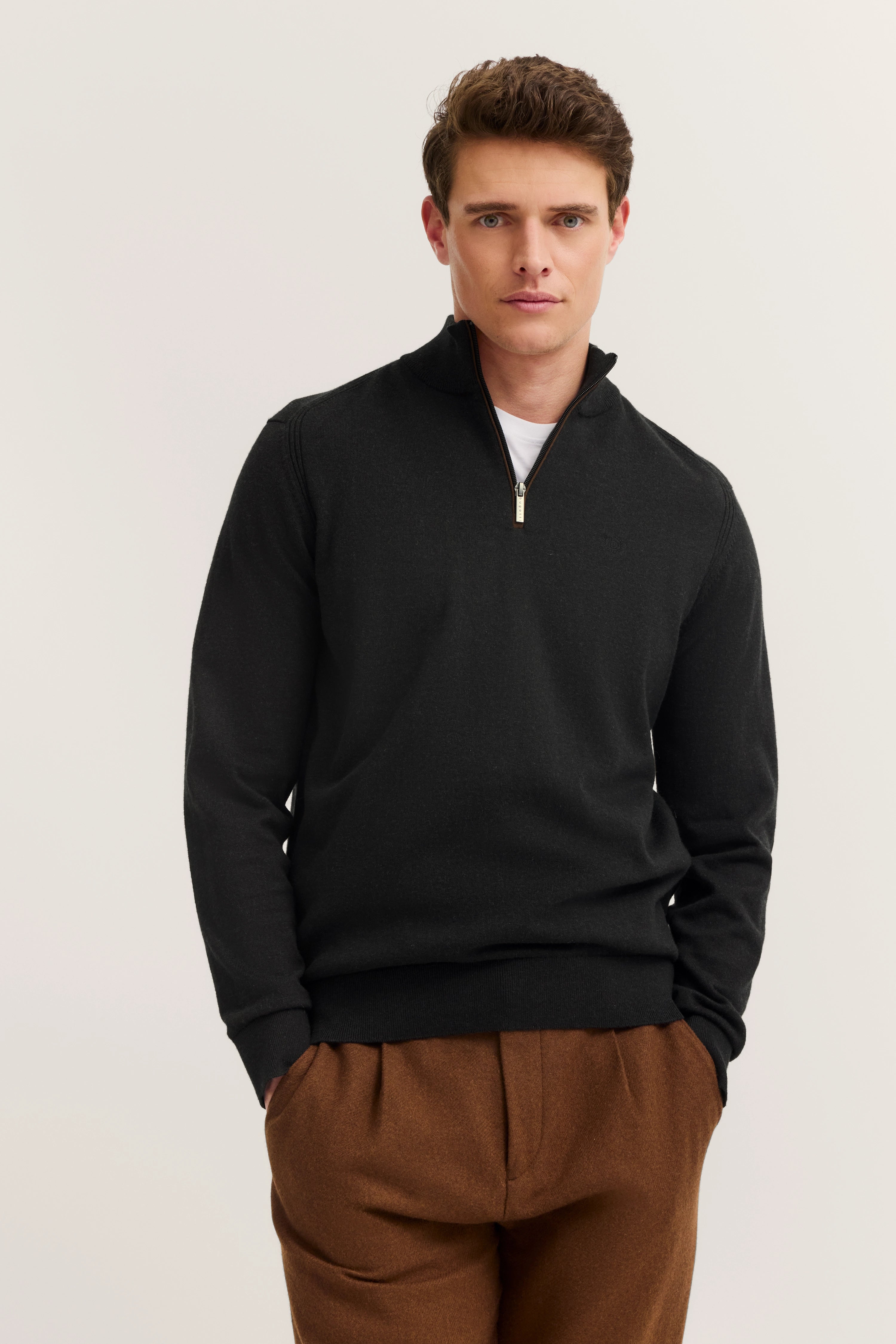 Schwarzer bugatti Pullover mit Reißverschluss, braune Hose, Modelbild mit legerem Posing.