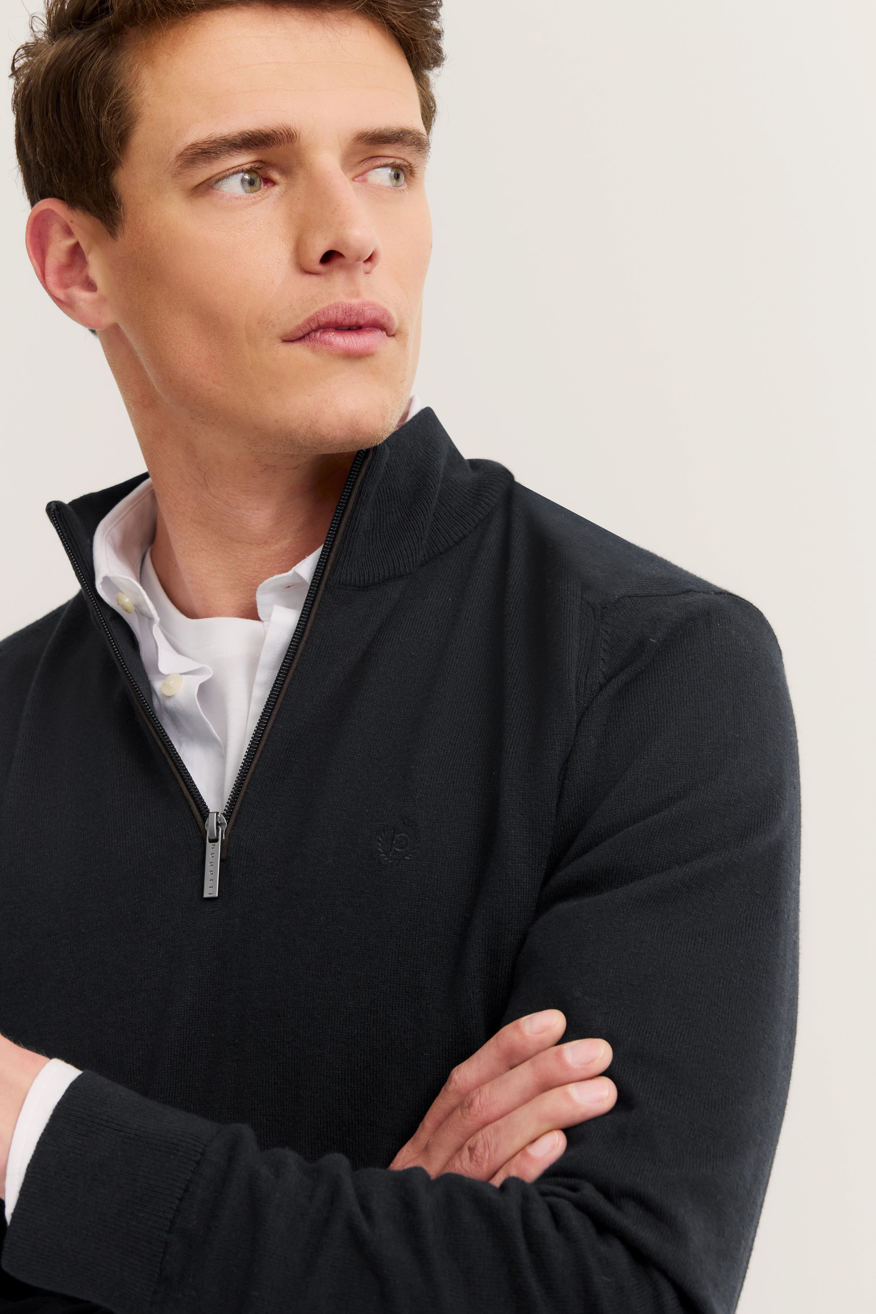 bugatti model: black zip-up sweater, white shirt, arms crossed, embodying Italian-inspired elegance and style.