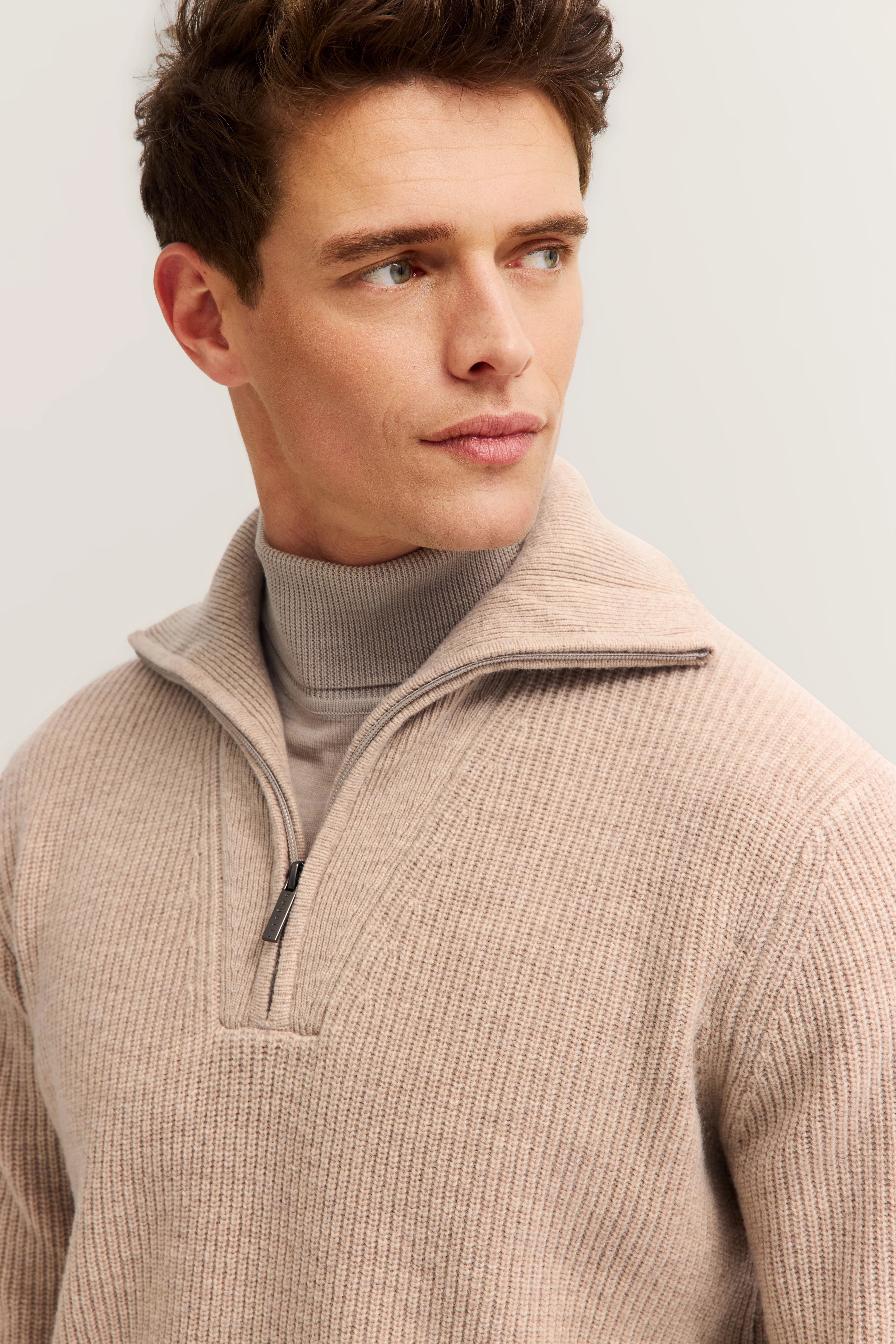 Beiger Strickpullover mit Zipper über grauem Rollkragen, Modelbild, Blick zur Seite.