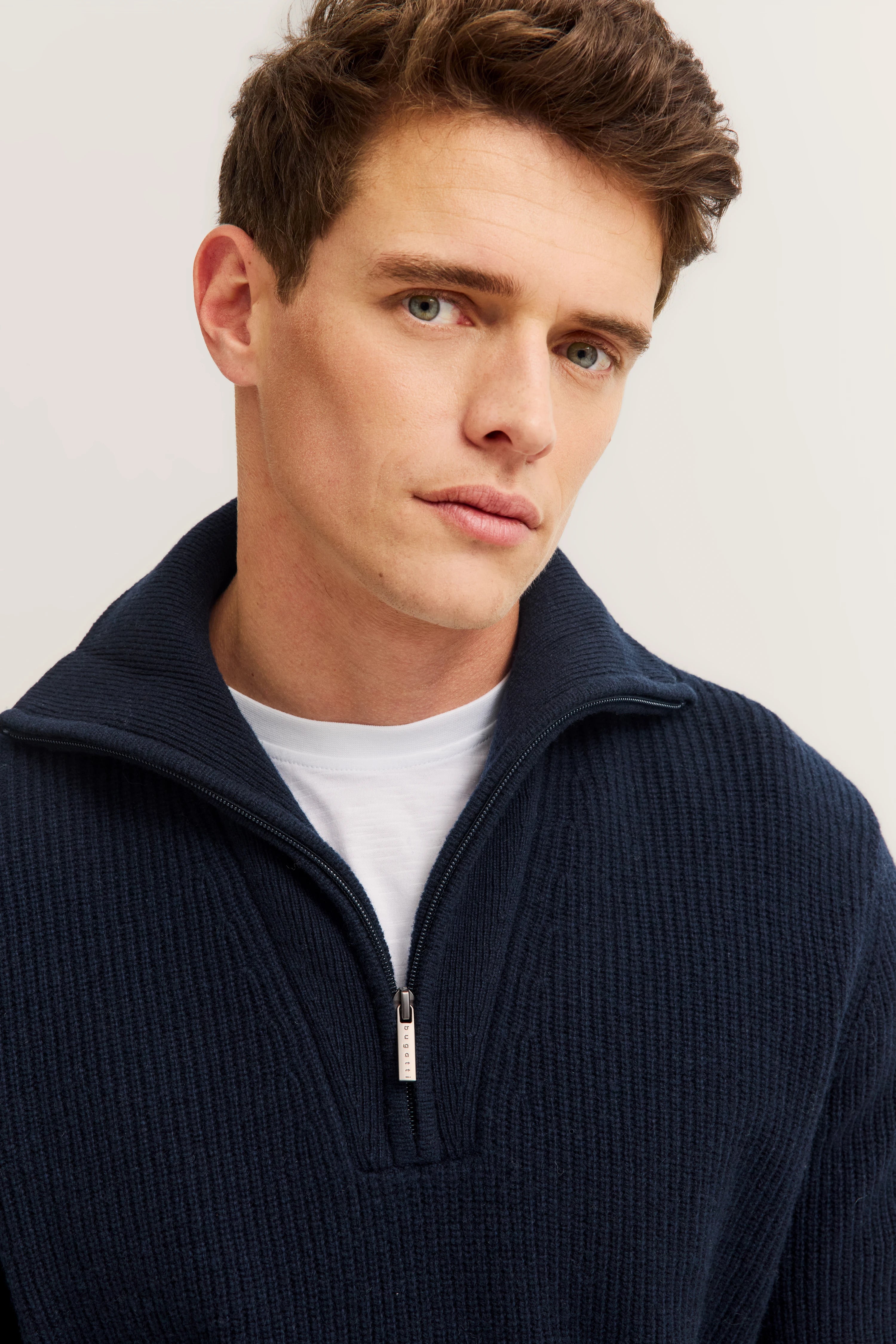 Bugatti Modelbild: Mann in blauem Strickpullover mit Reißverschluss, legeres Posing.