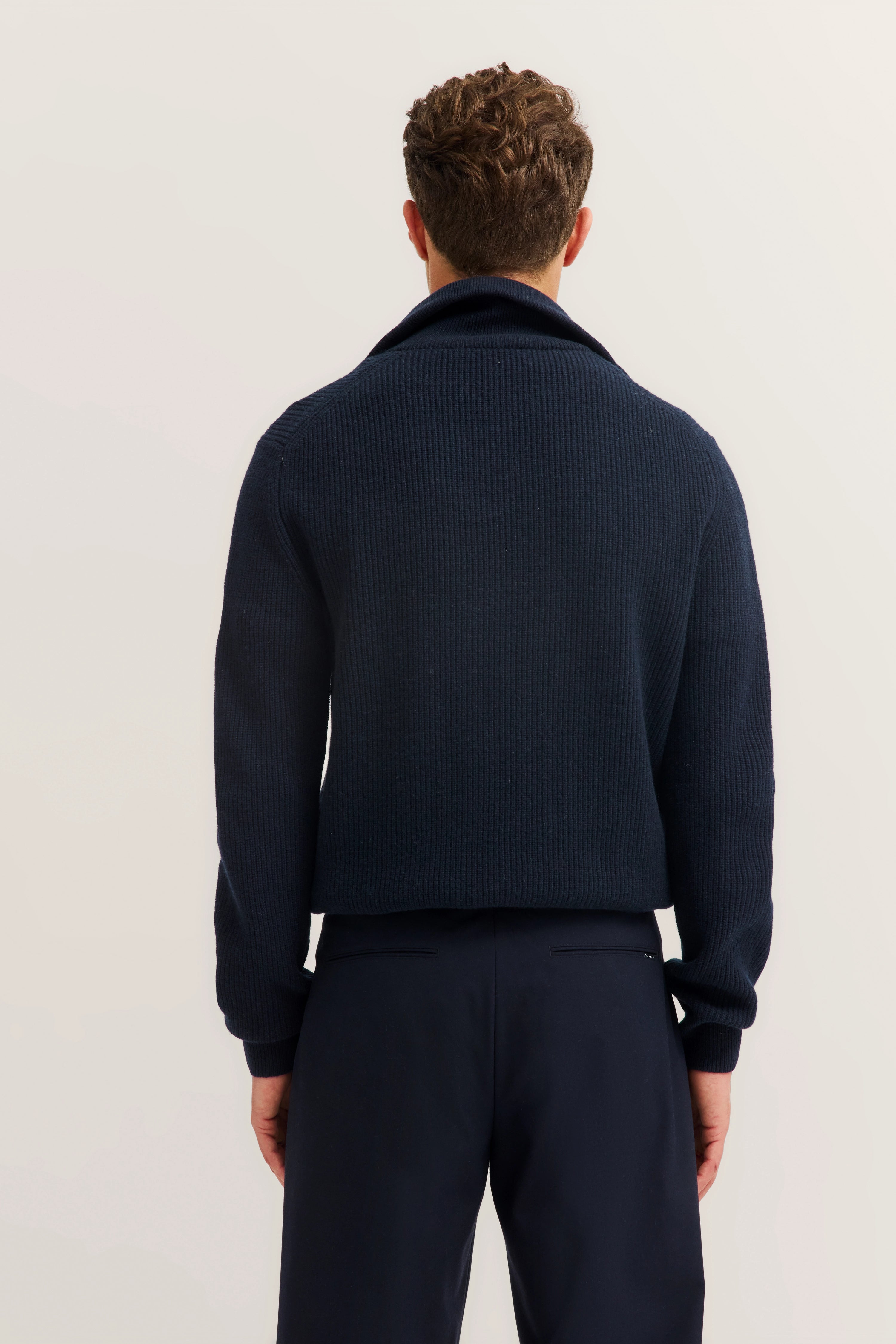 Navy cardigan and trousers, back view, model standing.