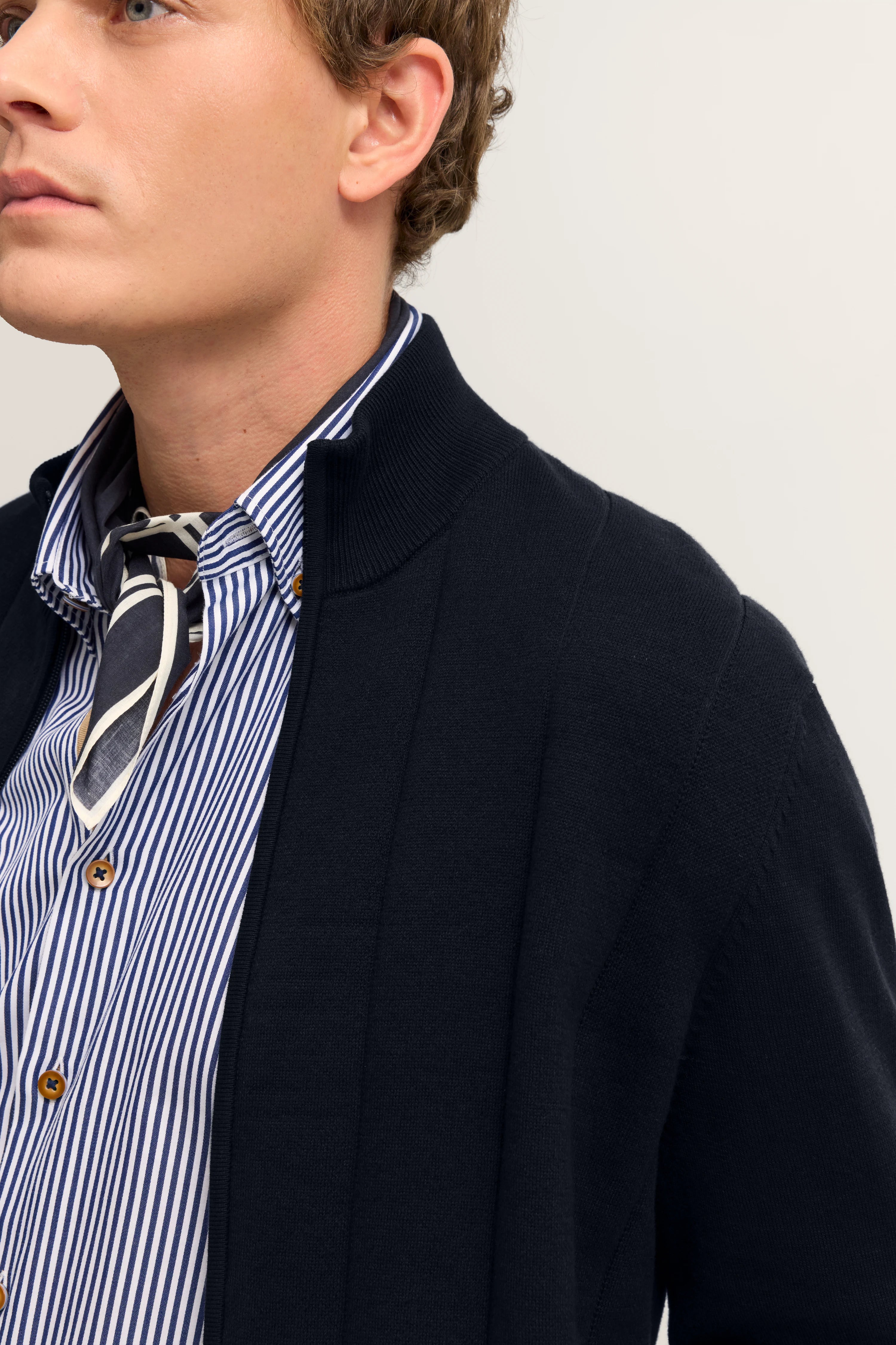 Bugatti Outfit: Dunkelblaue Strickjacke, blau-weiß gestreiftes Hemd, Büstenbild.