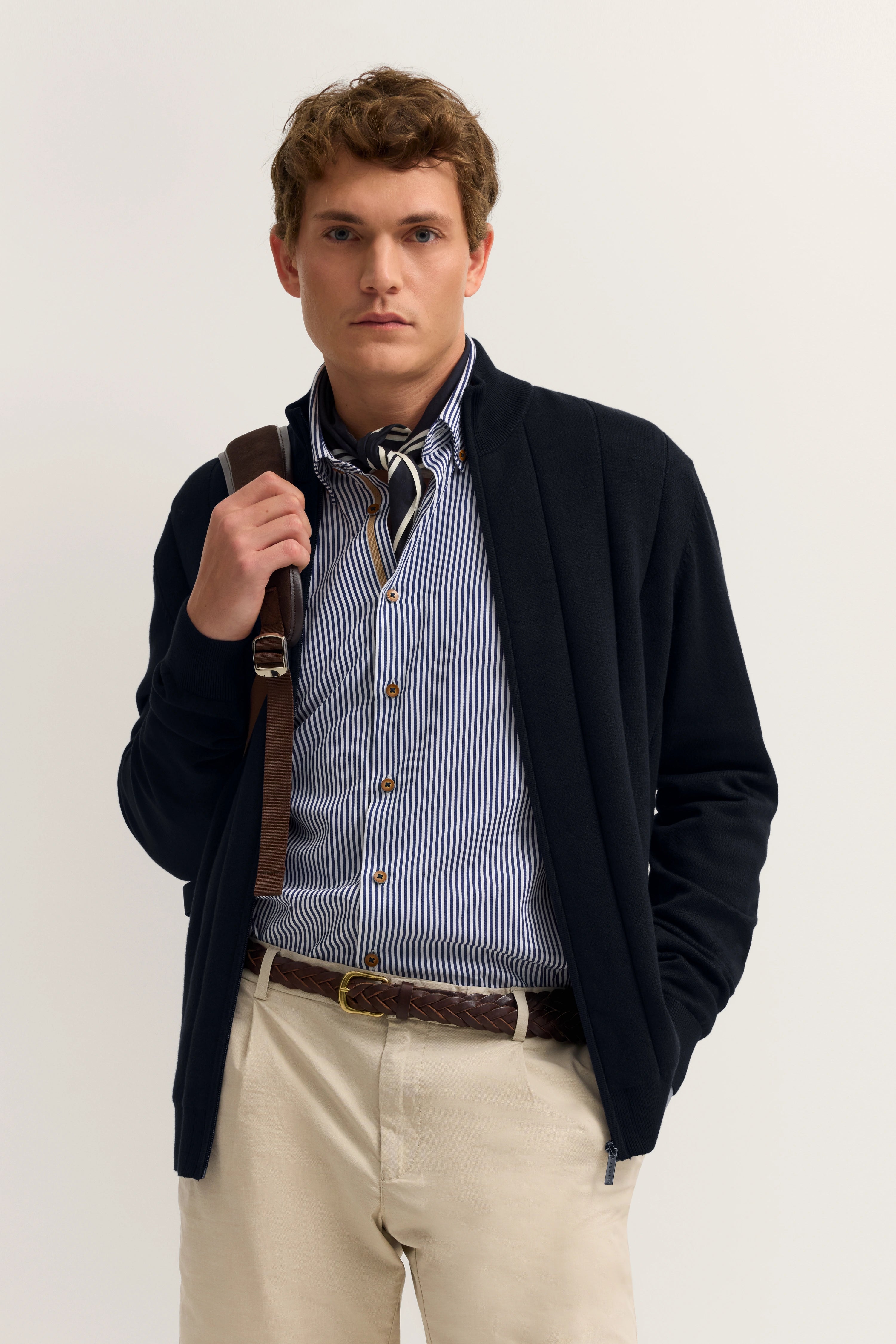 Model in navy Cardigan, gestreiftem Hemd und beigen Chinos. Lässig mit Hand in Tasche.