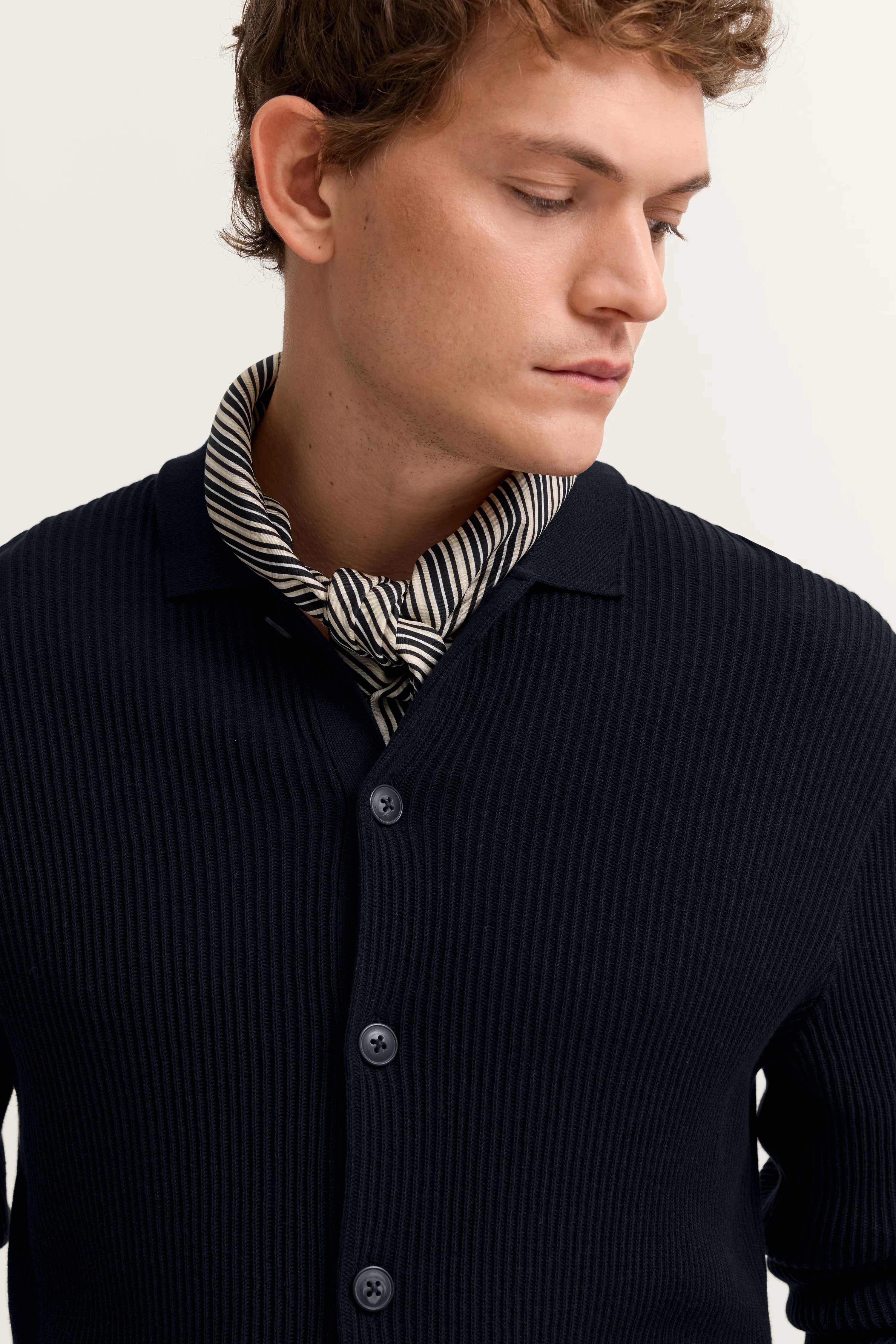 Model in dunkelblauer bugatti-Strickjacke mit gestreiftem Halstuch, Blick zur Seite.