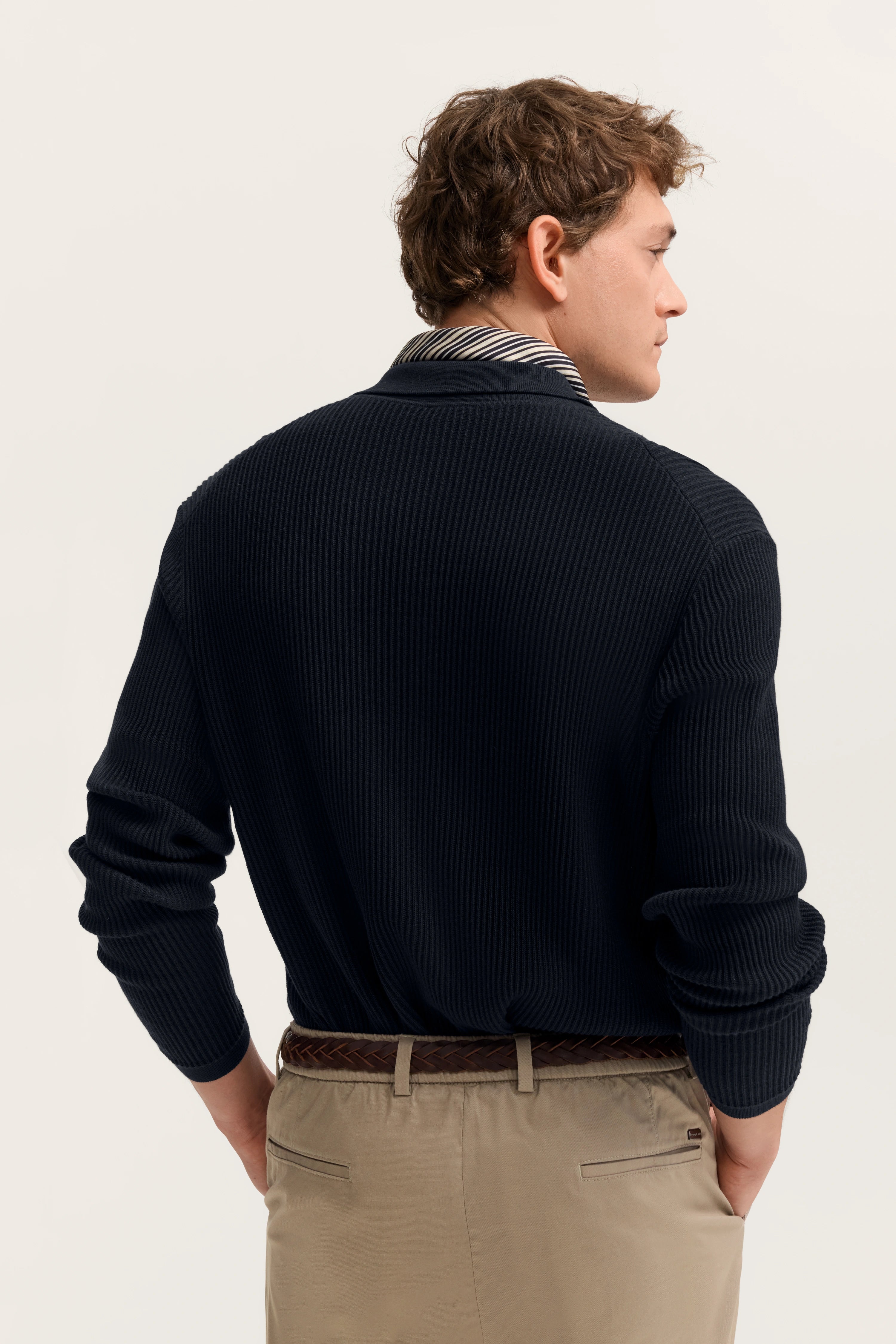 Model im dunklen Pullover mit gestreiftem Kragen, beige Hose, Rückenansicht.