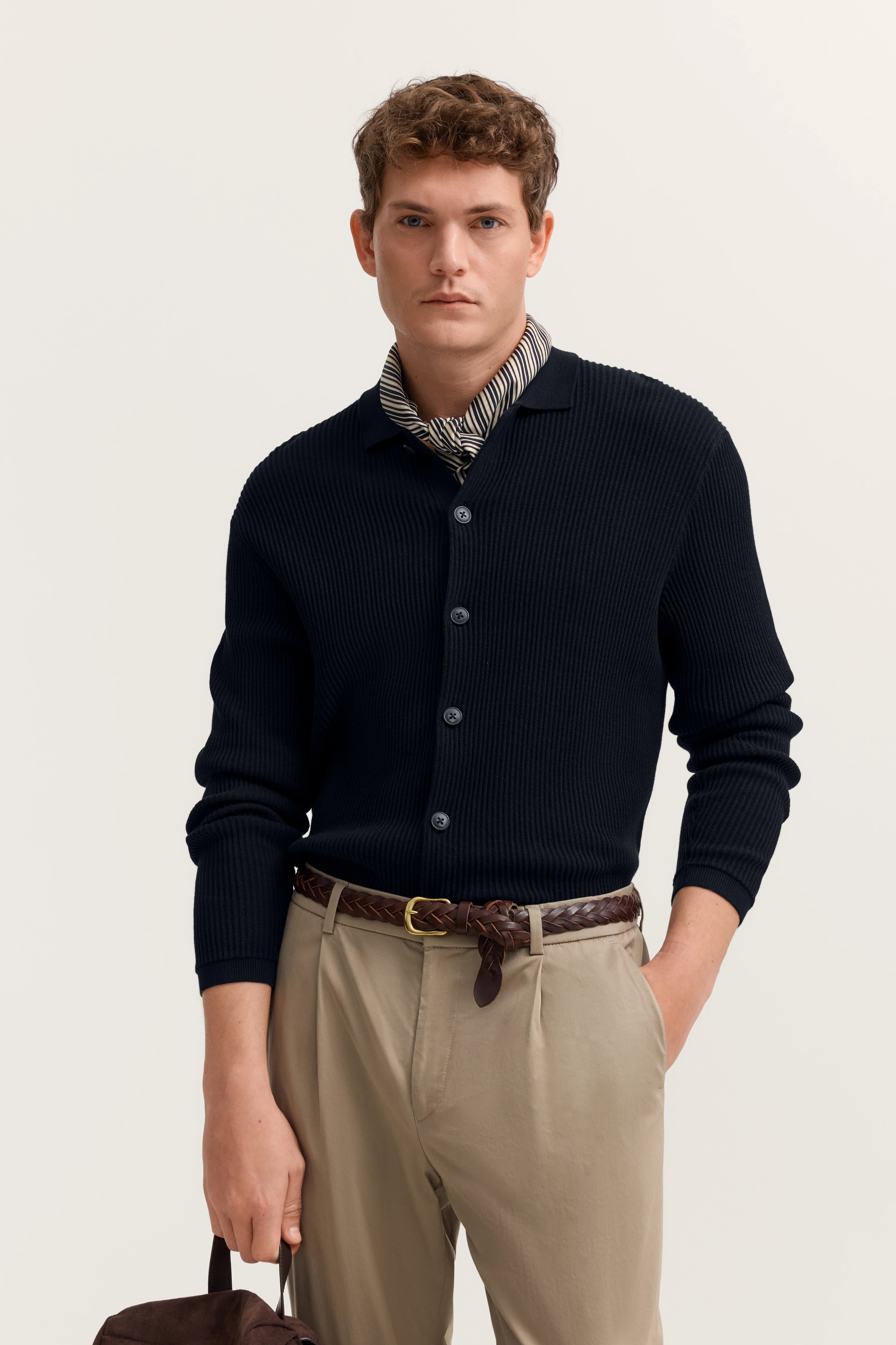 Model in dunkelblauer Strickjacke, gestreiftem Schal und beigefarbener Hose