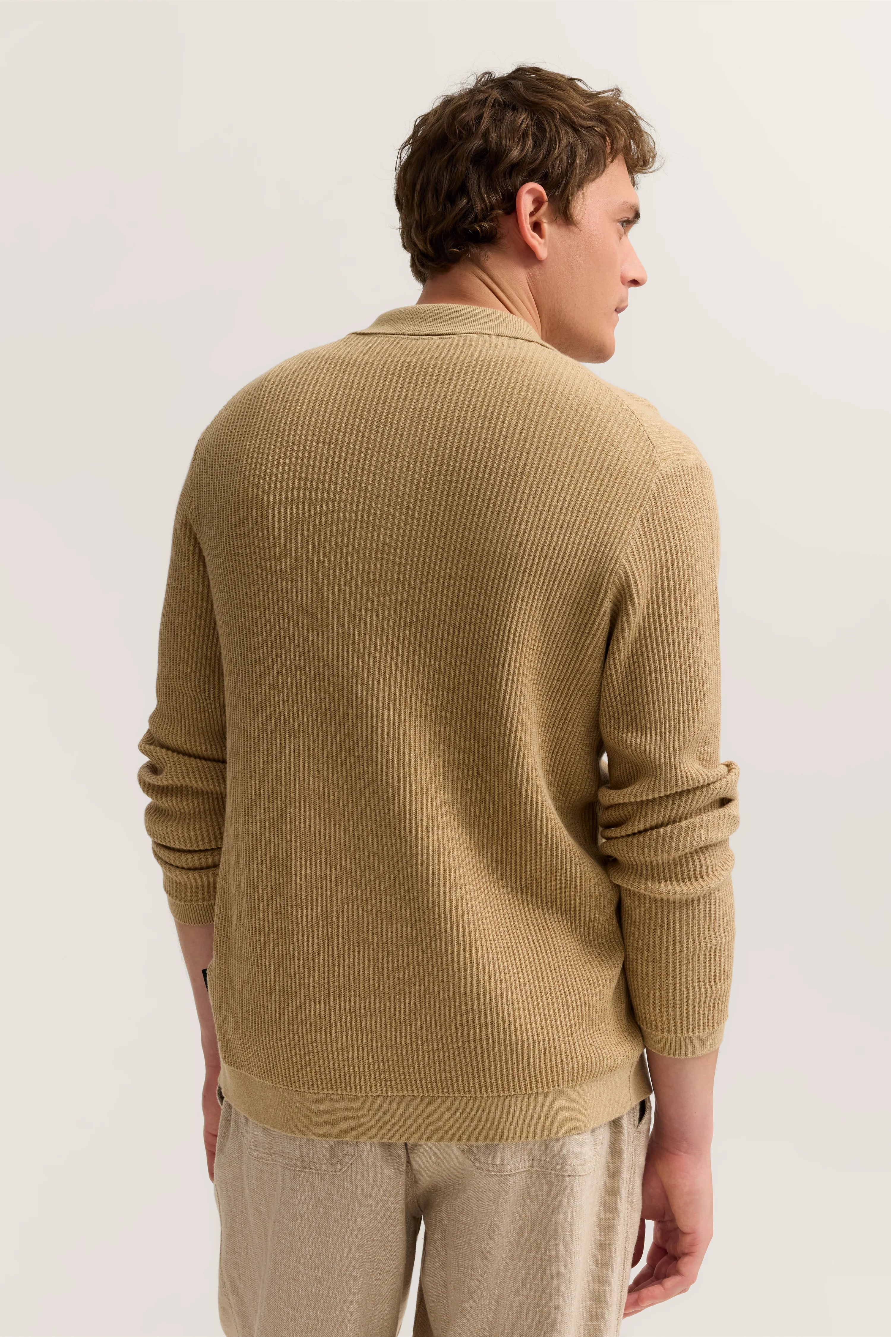 Beiges Strickpullover und Hose, Rückenansicht, Model steht entspannt.